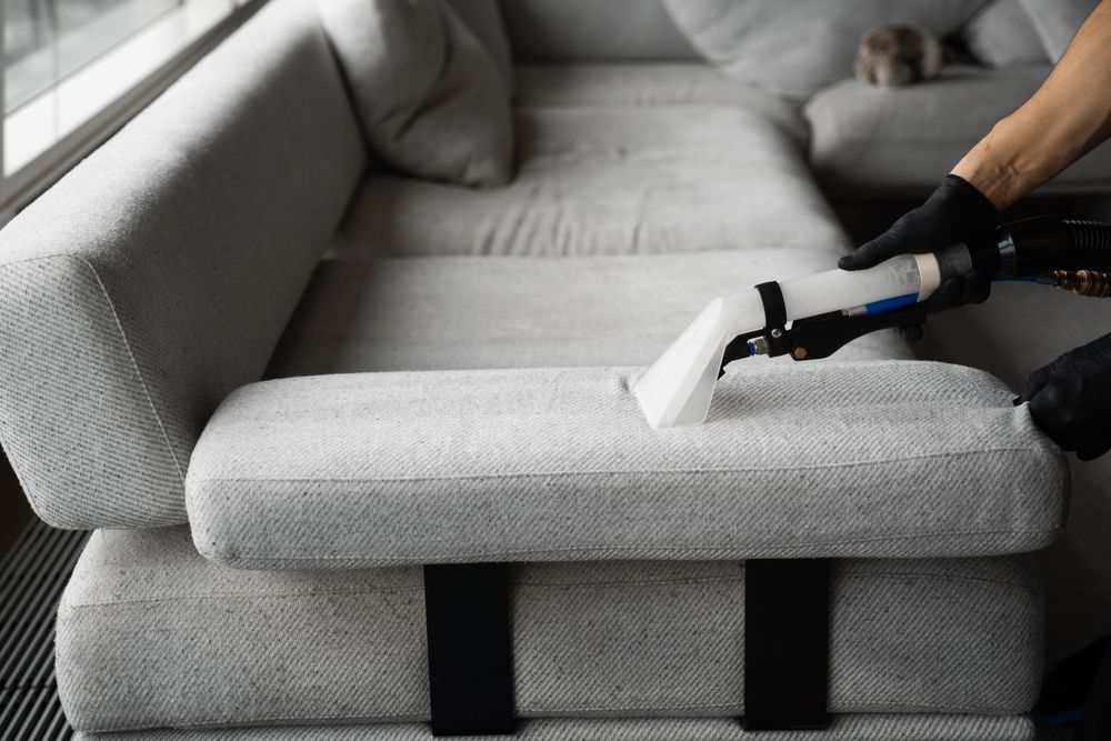 A person is cleaning a couch with a vacuum cleaner.