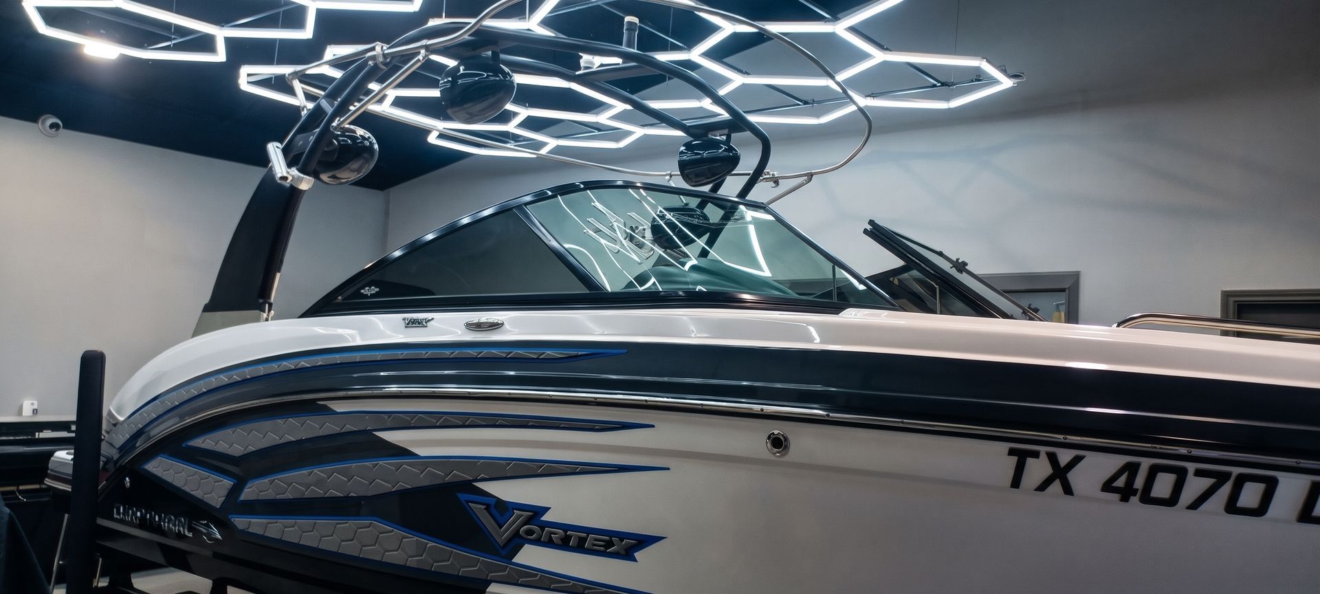 White and blue speedboat in a showroom under geometric ceiling lights