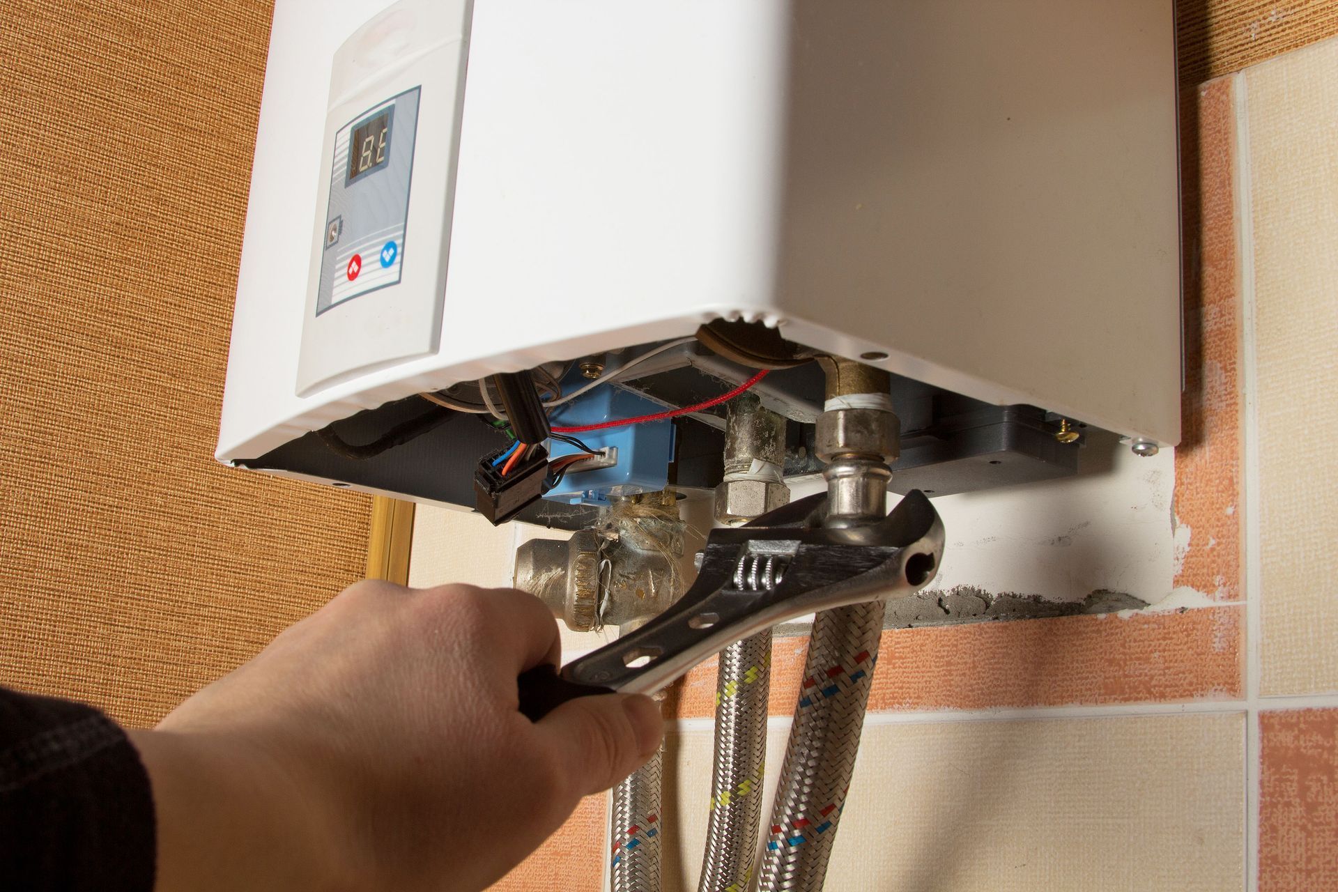 Hand tightening a wrench on the exposed underside of a wall-mounted boiler.
