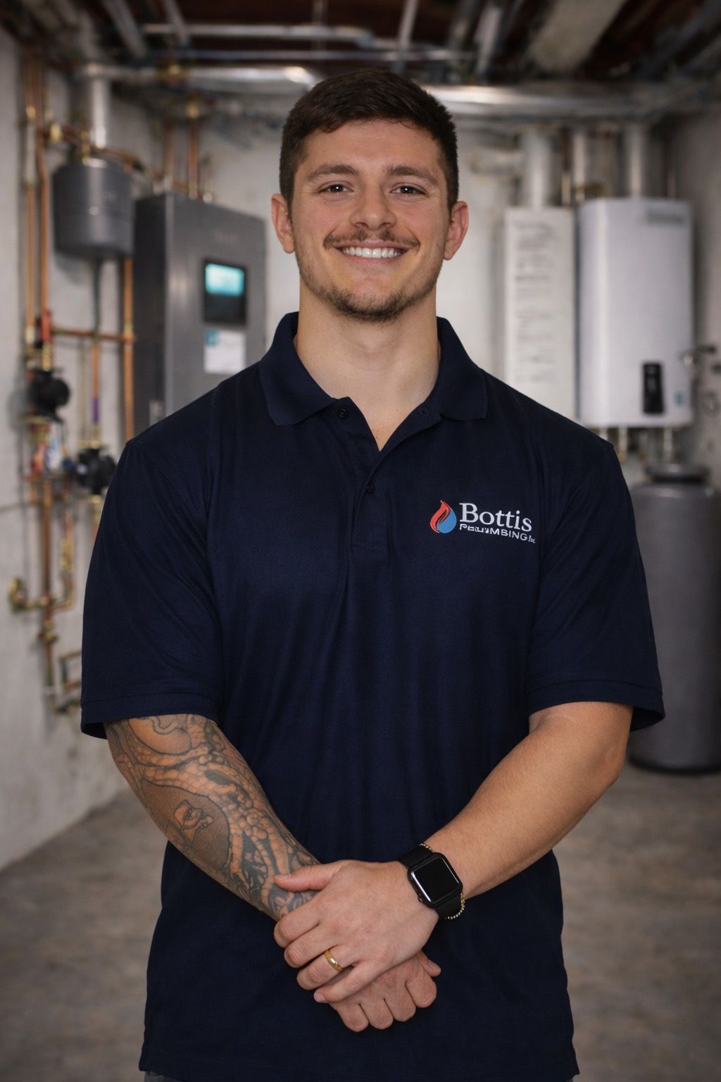 Smiling worker in a navy polo standing in an industrial facility with pipes and equipment behind him