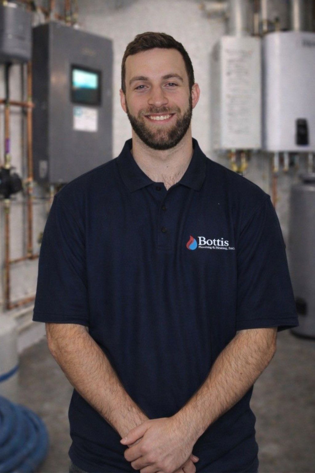 Smiling man in navy polo standing in an industrial facility with equipment in the background