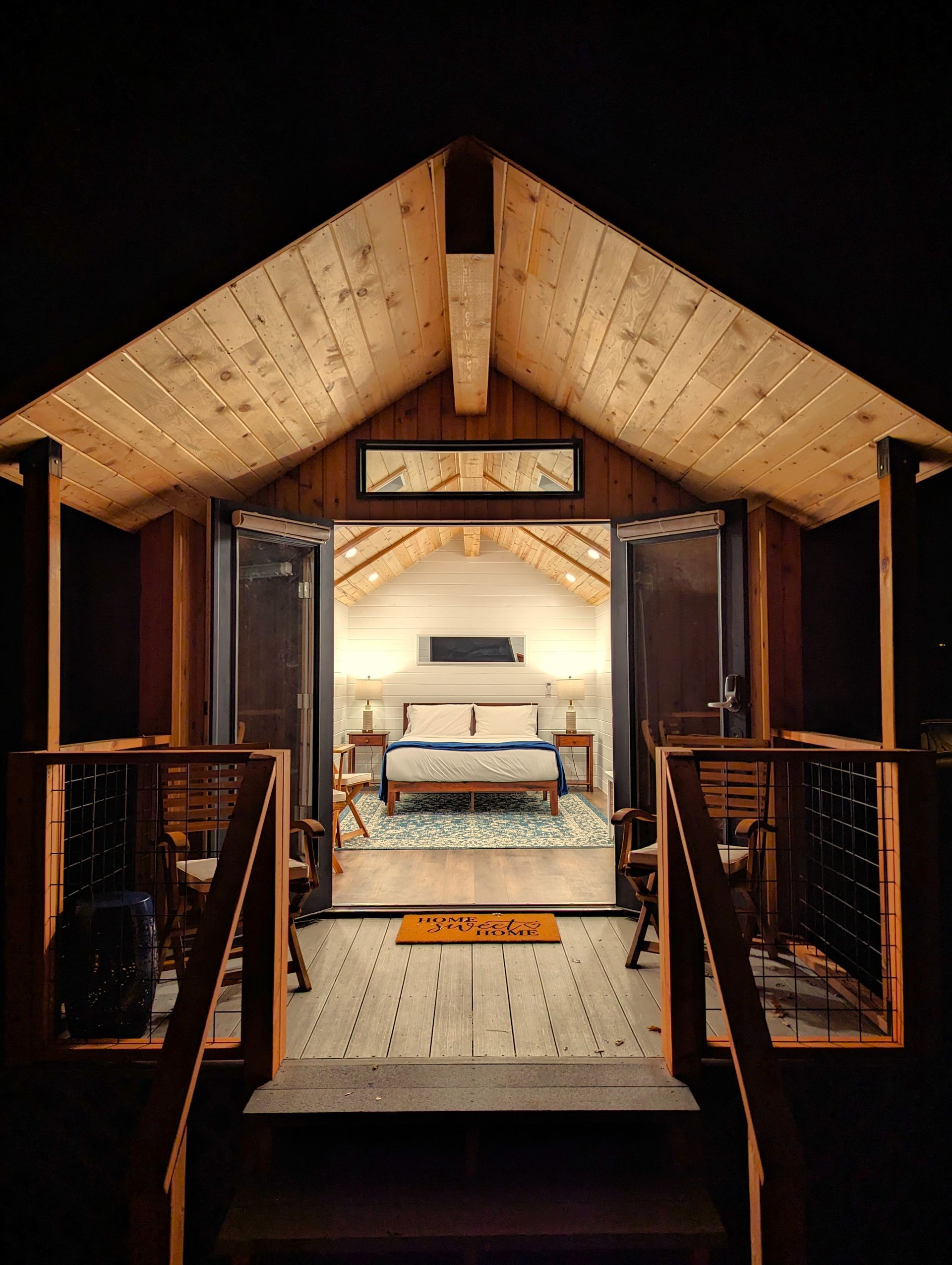A view of a bedroom from the porch of a cabin at night.