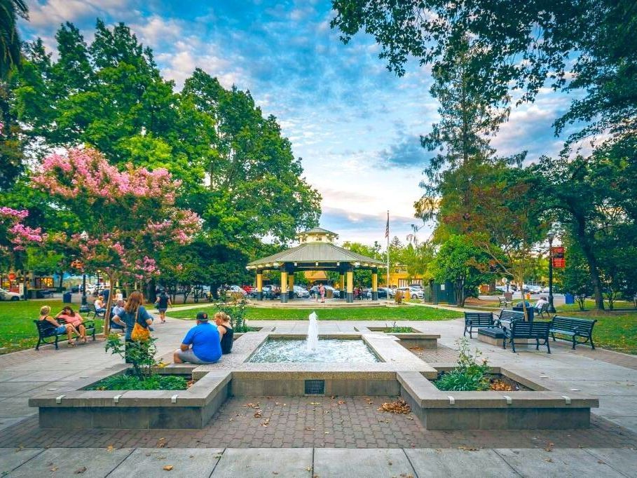 A group of people are sitting around a fountain in a park.