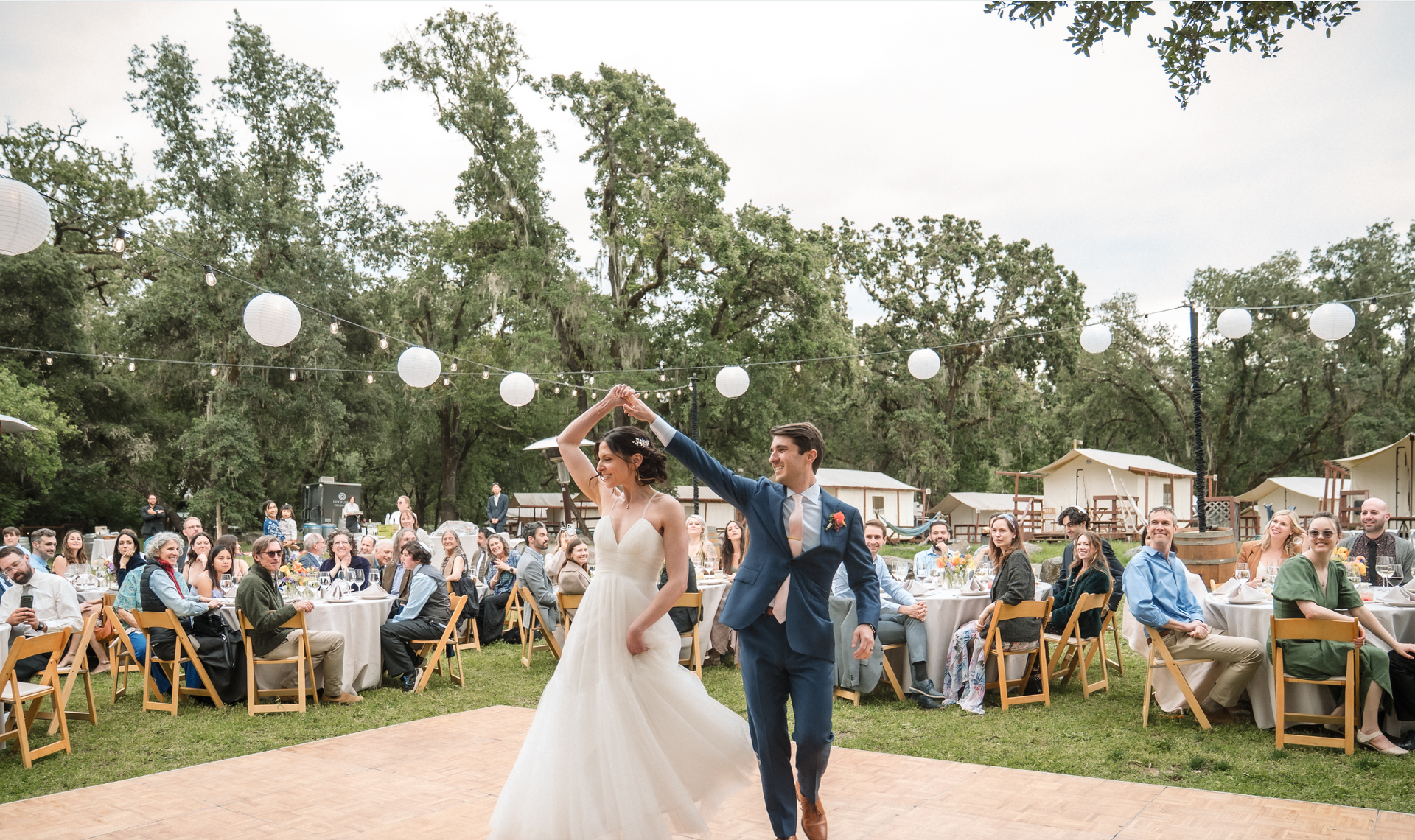 Husband and wife on dance floor with guests sitting a tables in the background