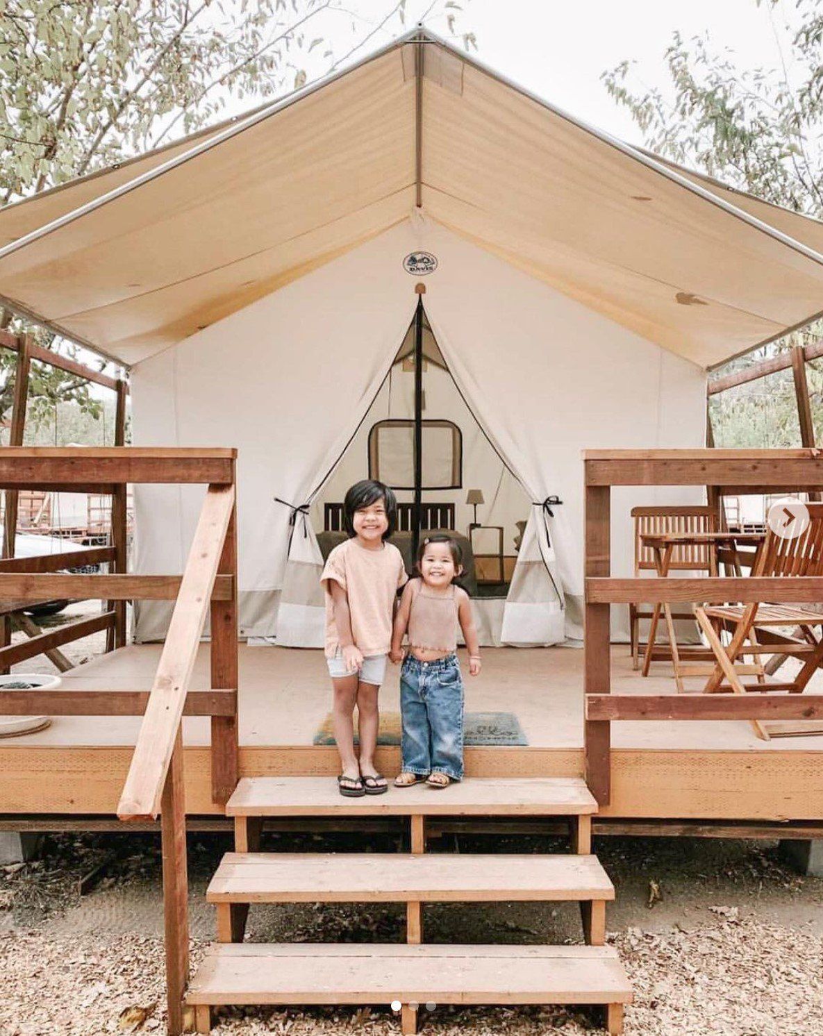 Two children are standing in front of a tent.