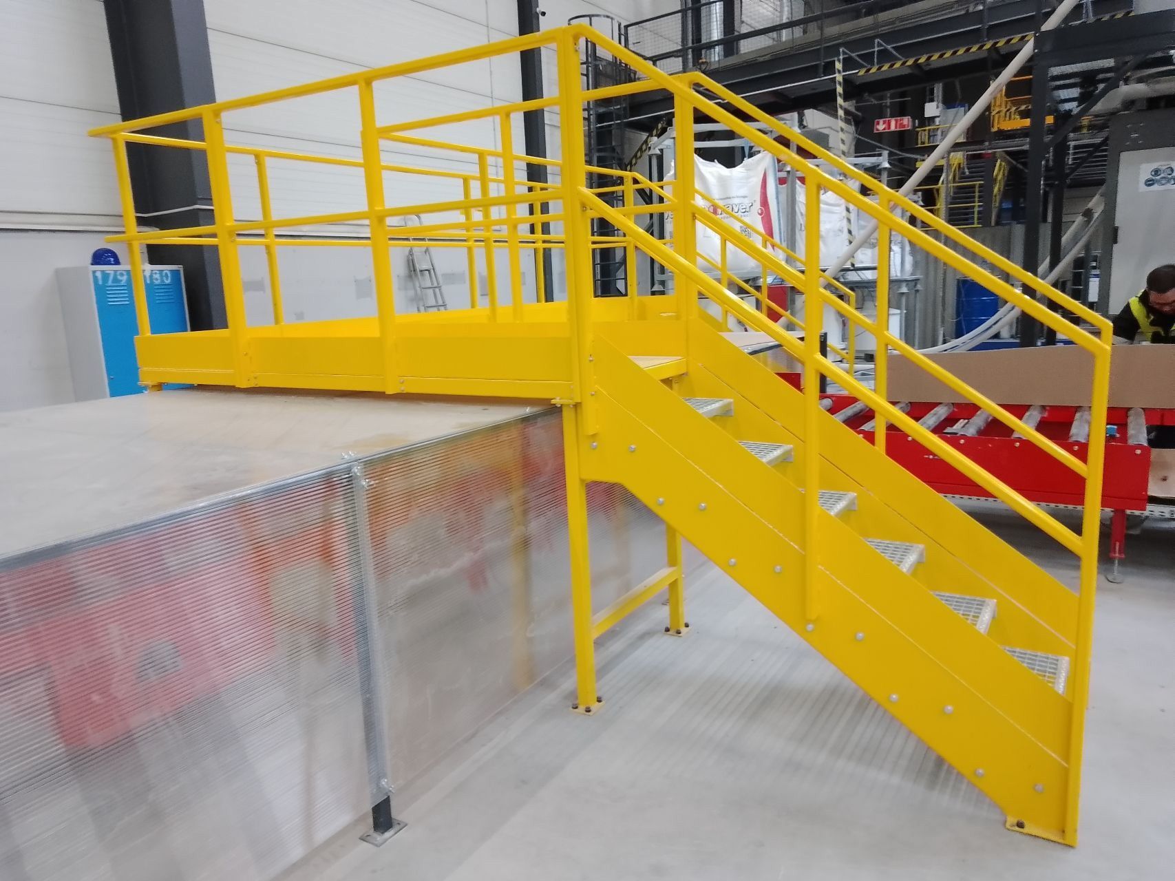 Industrial yellow steel platform with safety stairs, designed for ergonomic access over production lines in factory environment.