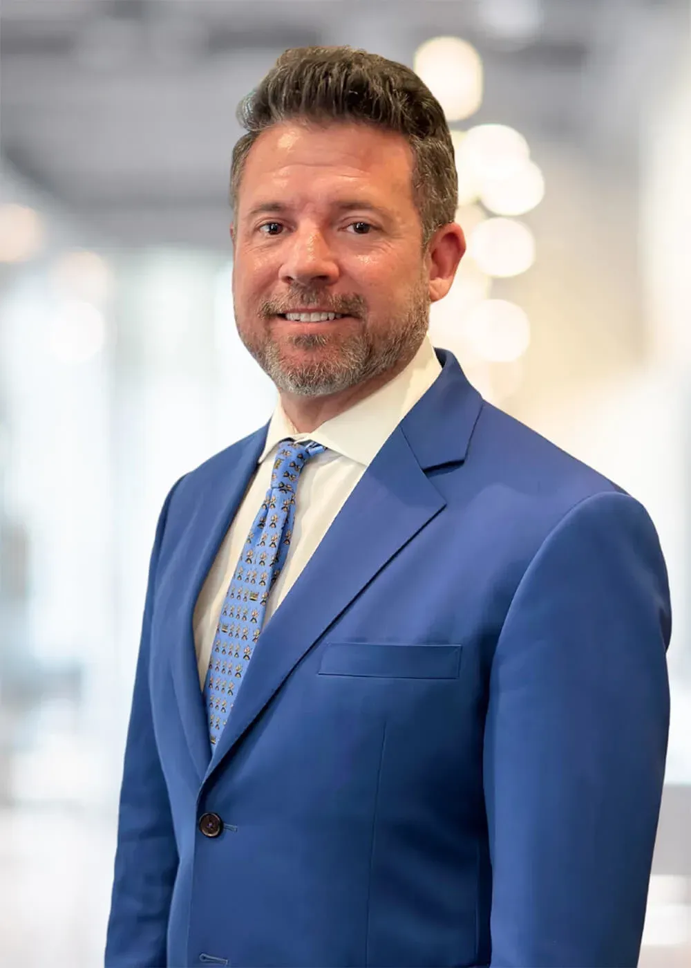 Man in blue suit, smiling. Blurred office background.