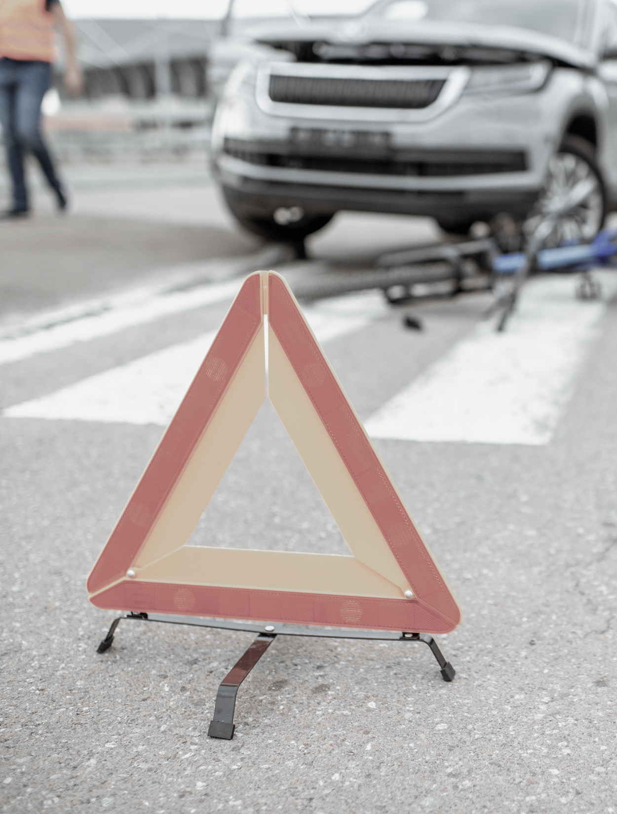 Warning triangle in foreground, car and bicycle accident scene blurred in background.