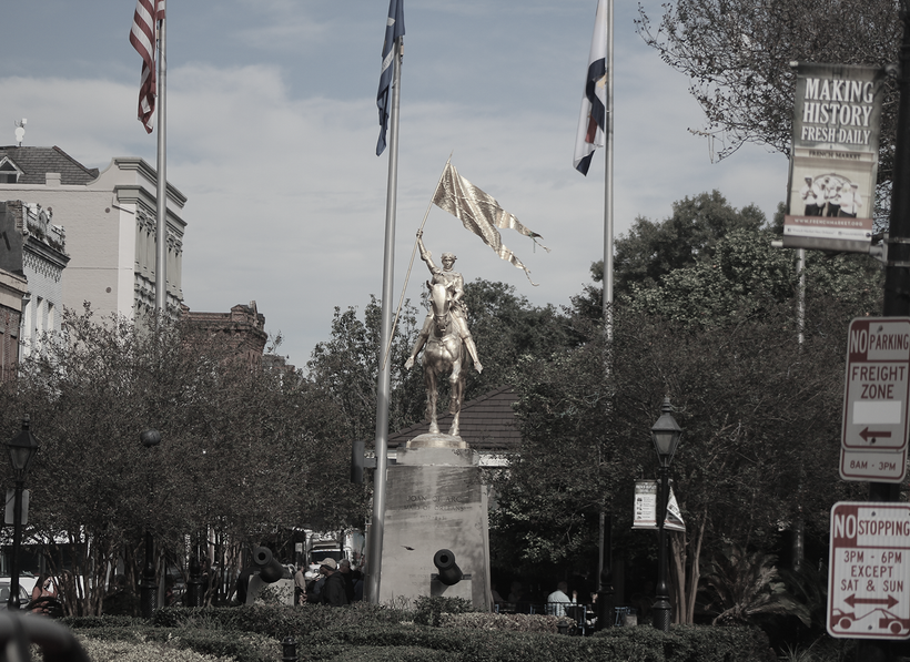 Statue of a man on a horse holding a banner, with flags and trees in the background.