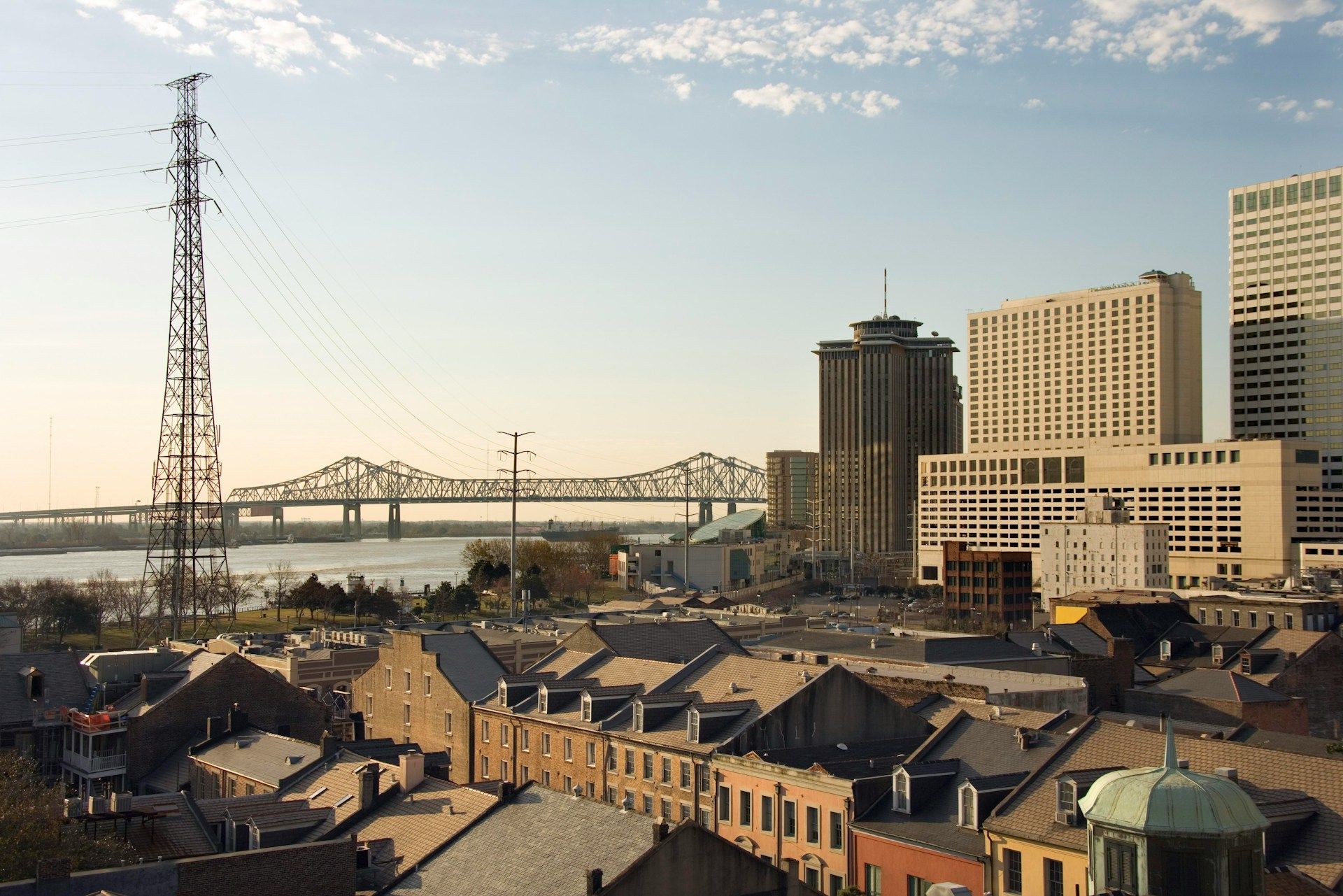 Cityscape of New Orleans with power lines, bridge, buildings, and river on a sunny day.
