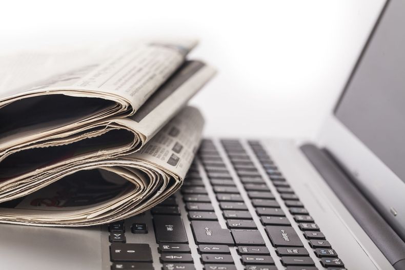 Newspapers stacked on a laptop keyboard. White background.
