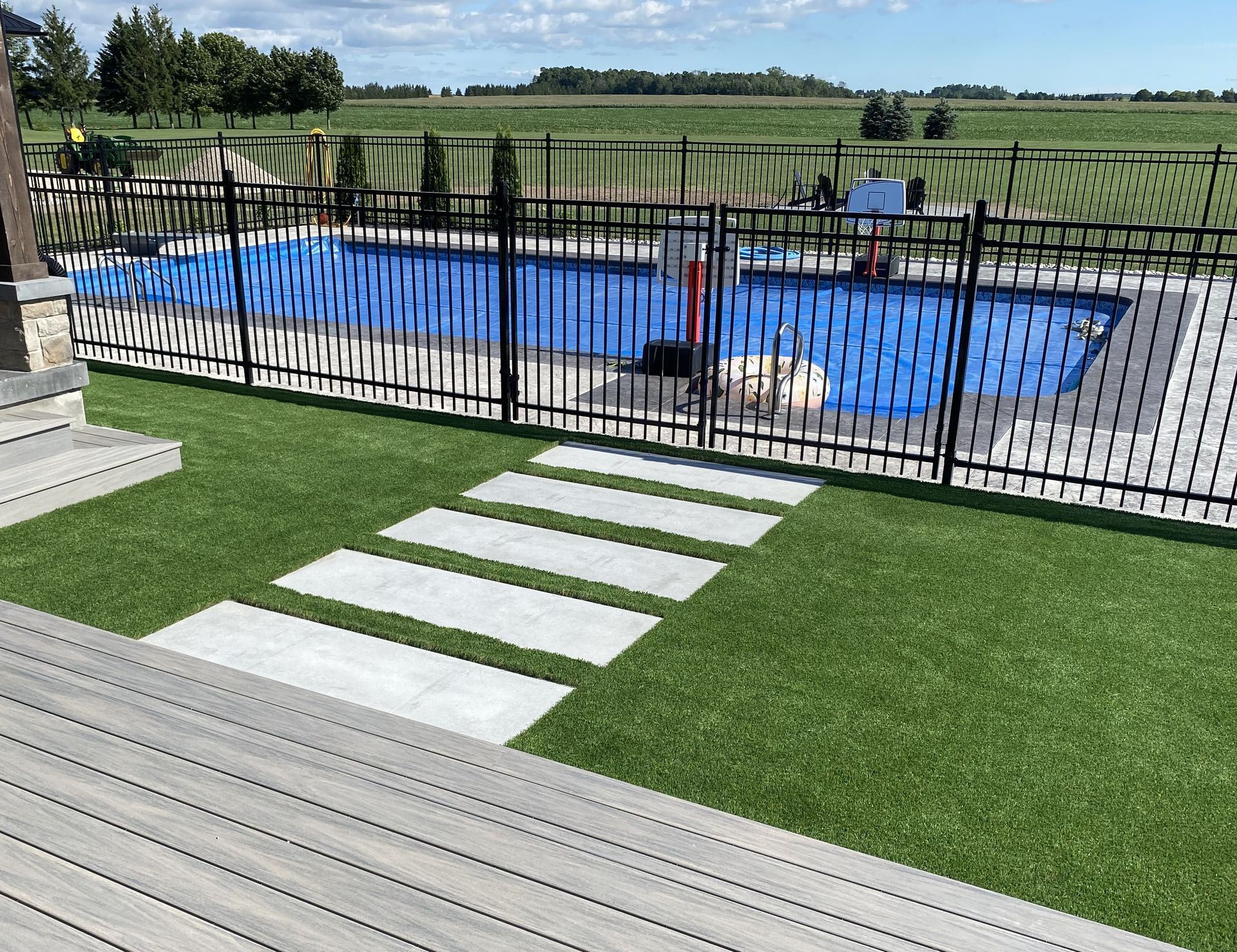 Backyard with rectangular pool, stepping stones on green turf, and fields in the background.