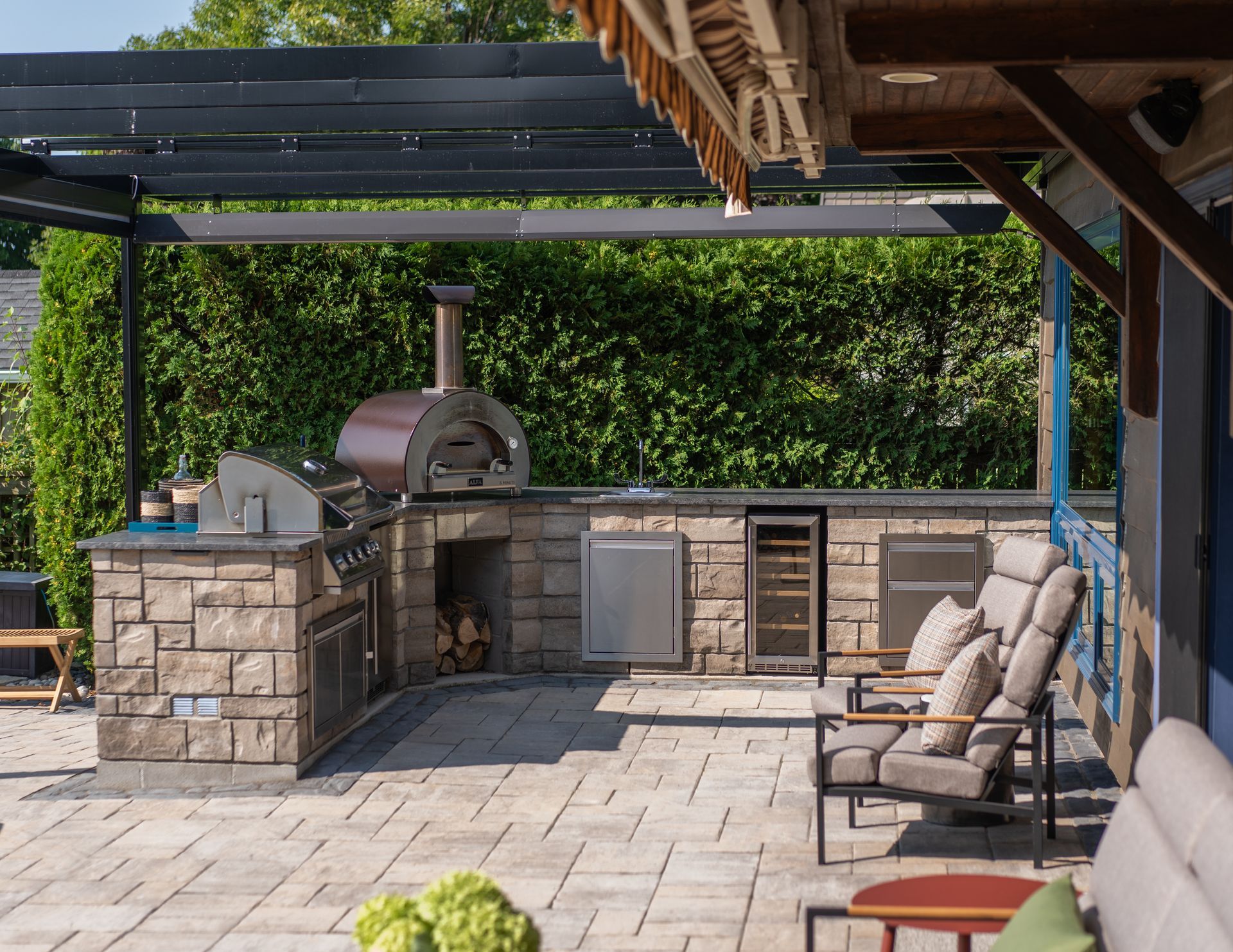 Outdoor kitchen with stone counters, pizza oven, grill, and seating.