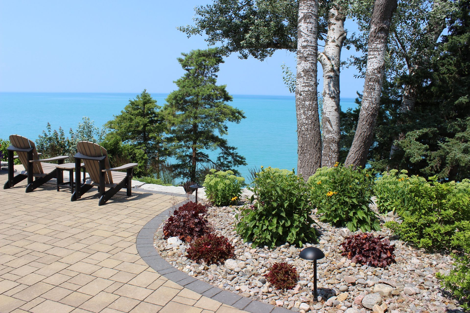 Patio overlooking a blue lake with Adirondack chairs, trees, and landscaping.