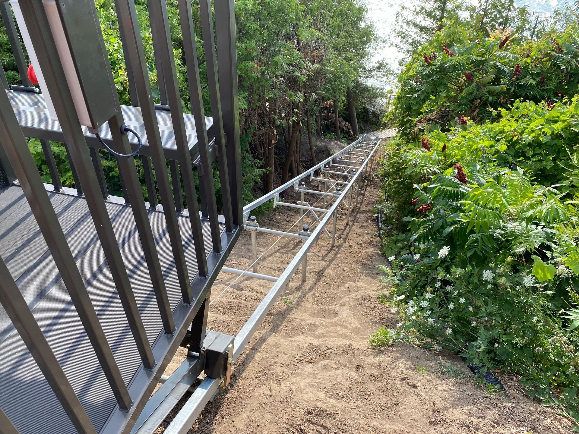 A metal gate partially open with a metal track on the ground, leading into a wooded area.