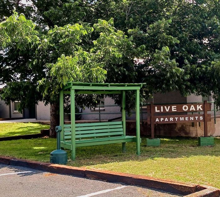 Live Oak Apartments sign beside a green bus shelter under trees