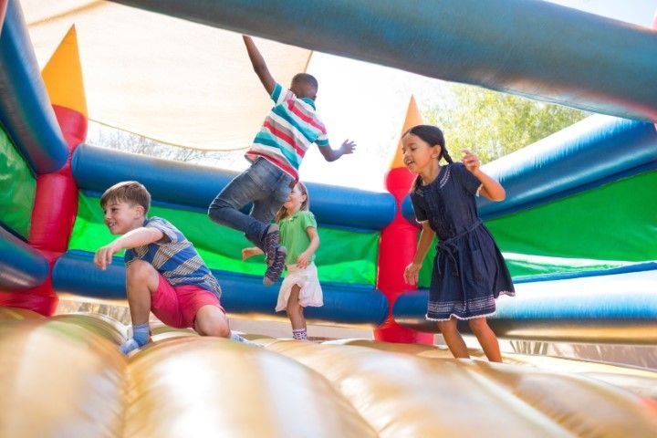 Children playing on a colorful inflatable bounce house outdoors.