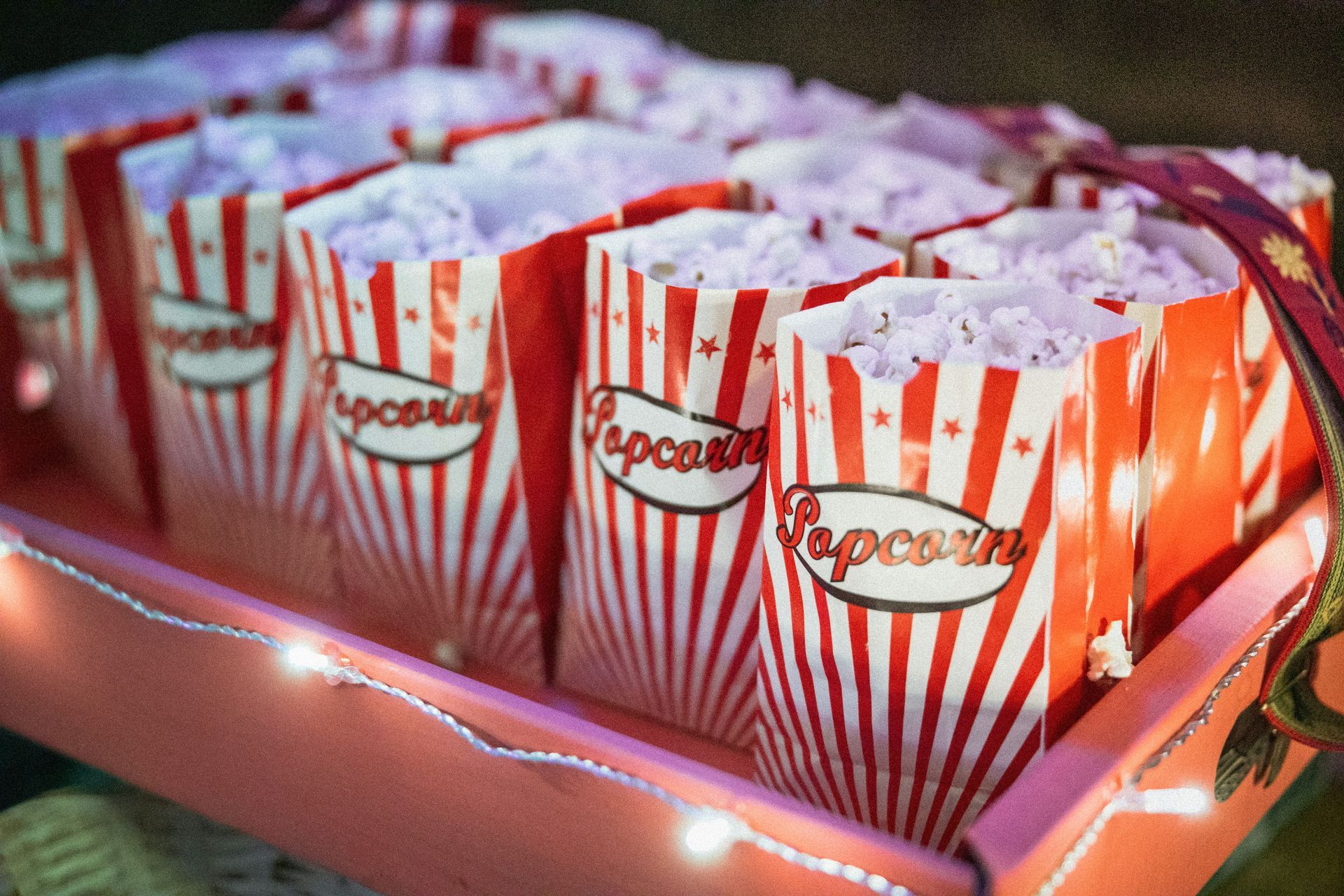Red-and-white striped popcorn boxes lined up on a tray with purple string lights