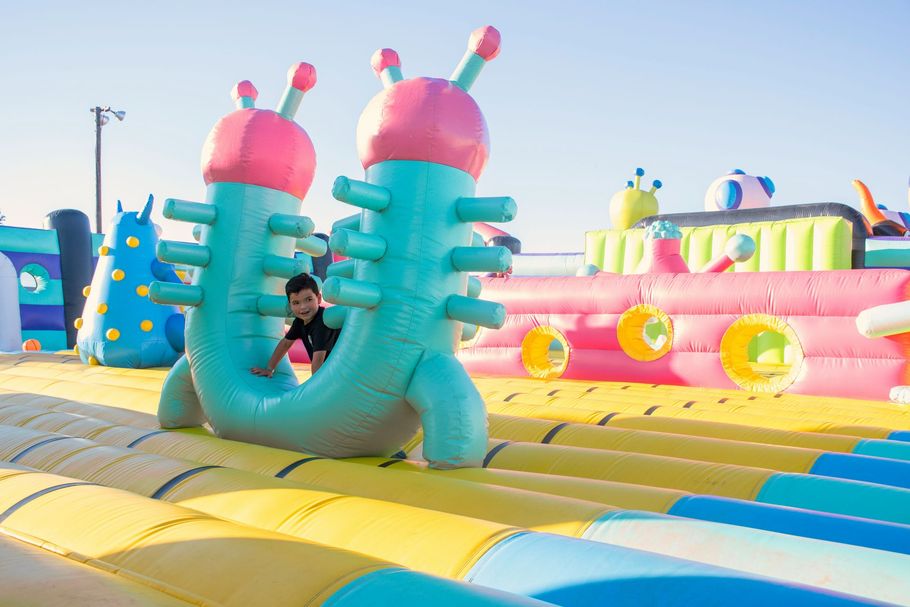 Colorful inflatable playground with a child sliding through a turquoise arch under a sunny sky