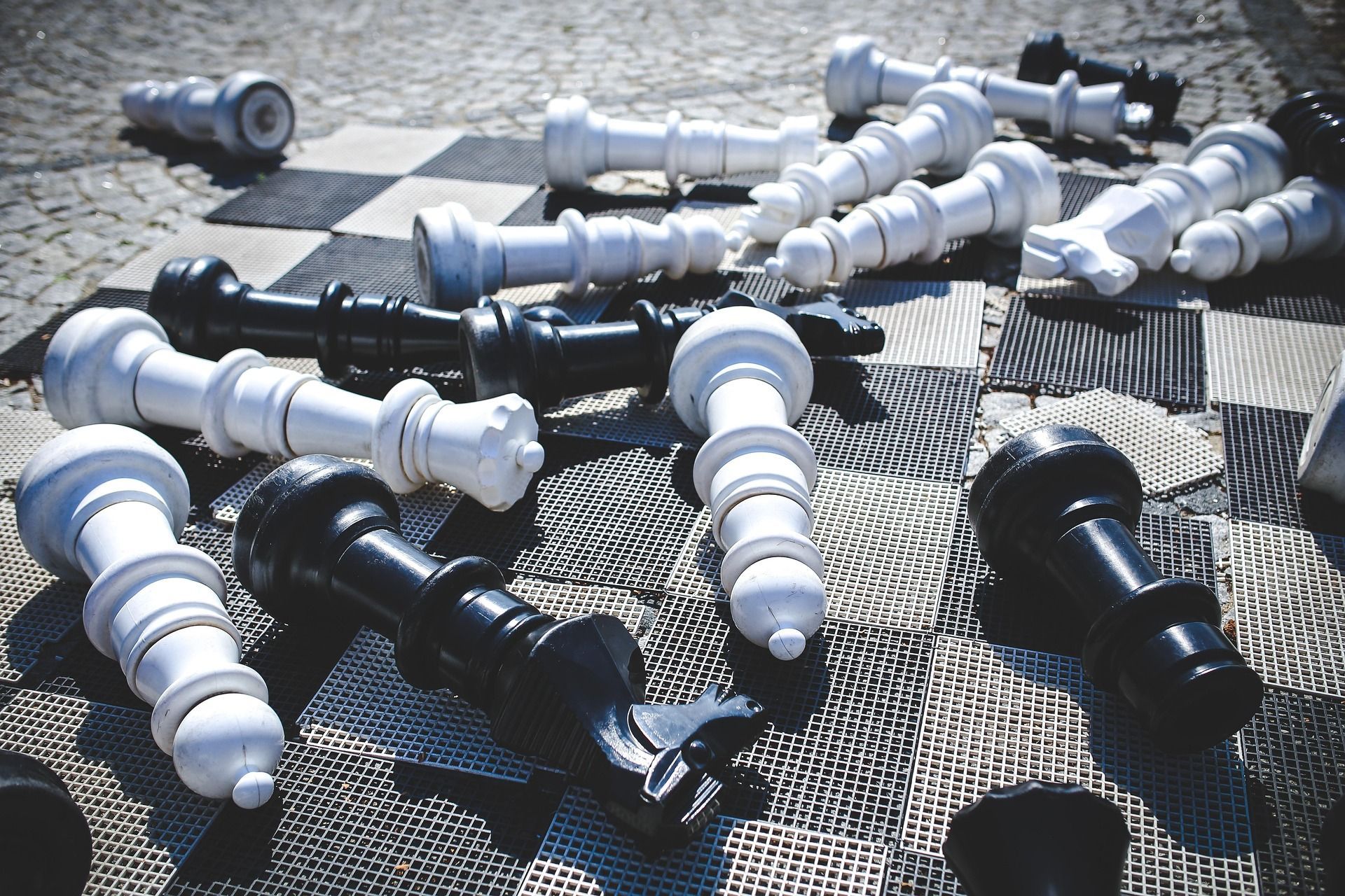Scattered white and black chess pieces on a woven mat, with several pieces lying on their sides