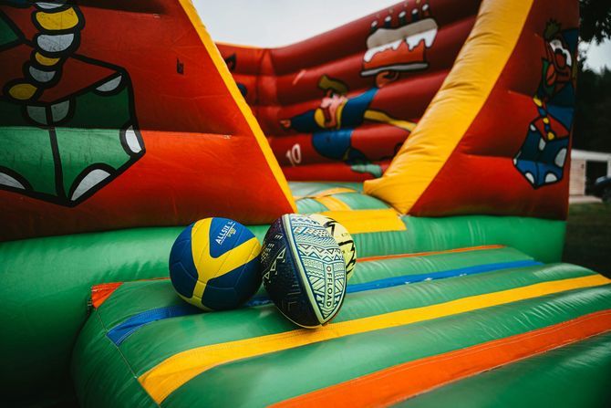 Two colorful balls on a striped inflatable bounce house with red walls and cartoon graphics.
