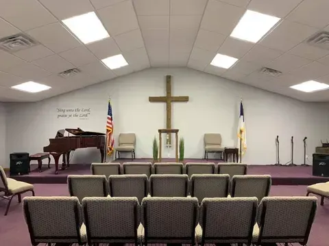 Church sanctuary with cross on stage, rows of chairs, podium, and American flag under bright ceiling lights