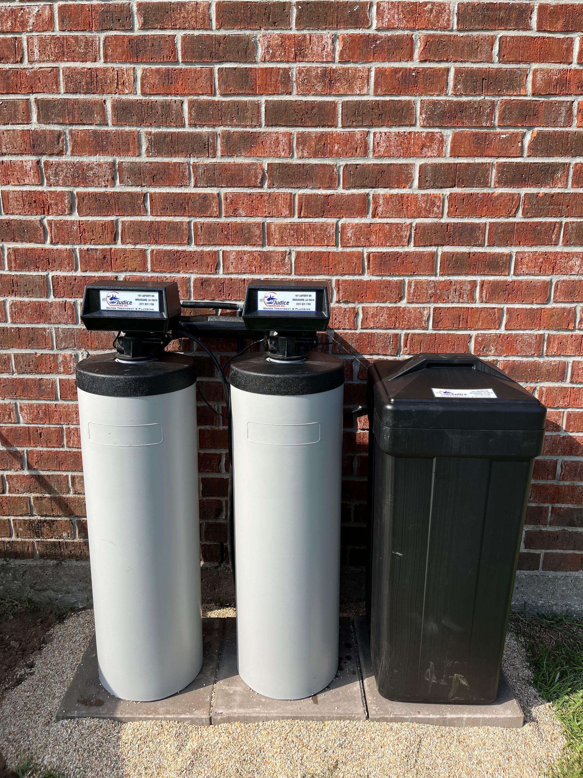 Two gray water treatment tanks and a black salt tank against a brick wall.