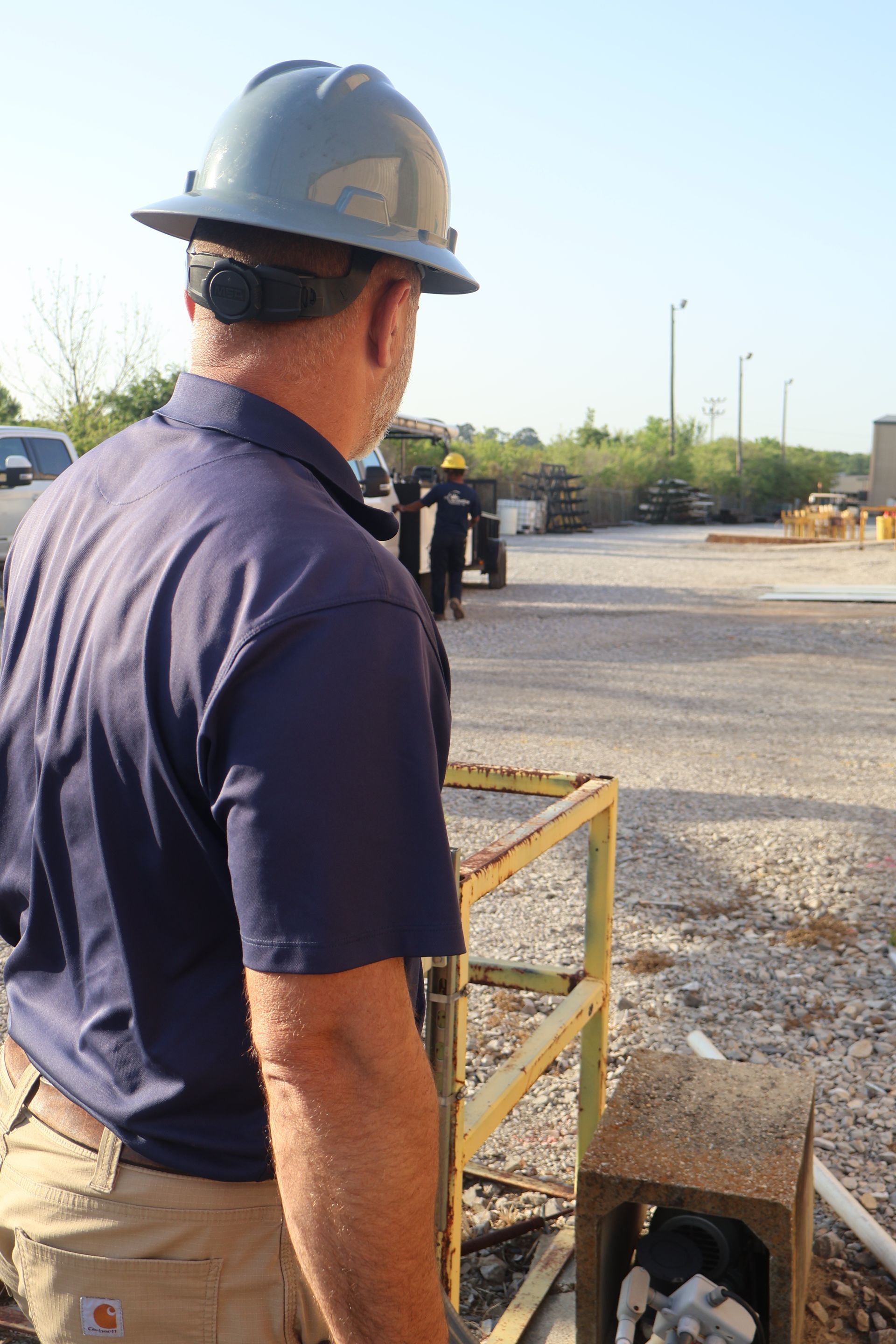 Man in hard hat looks towards industrial area with other workers.