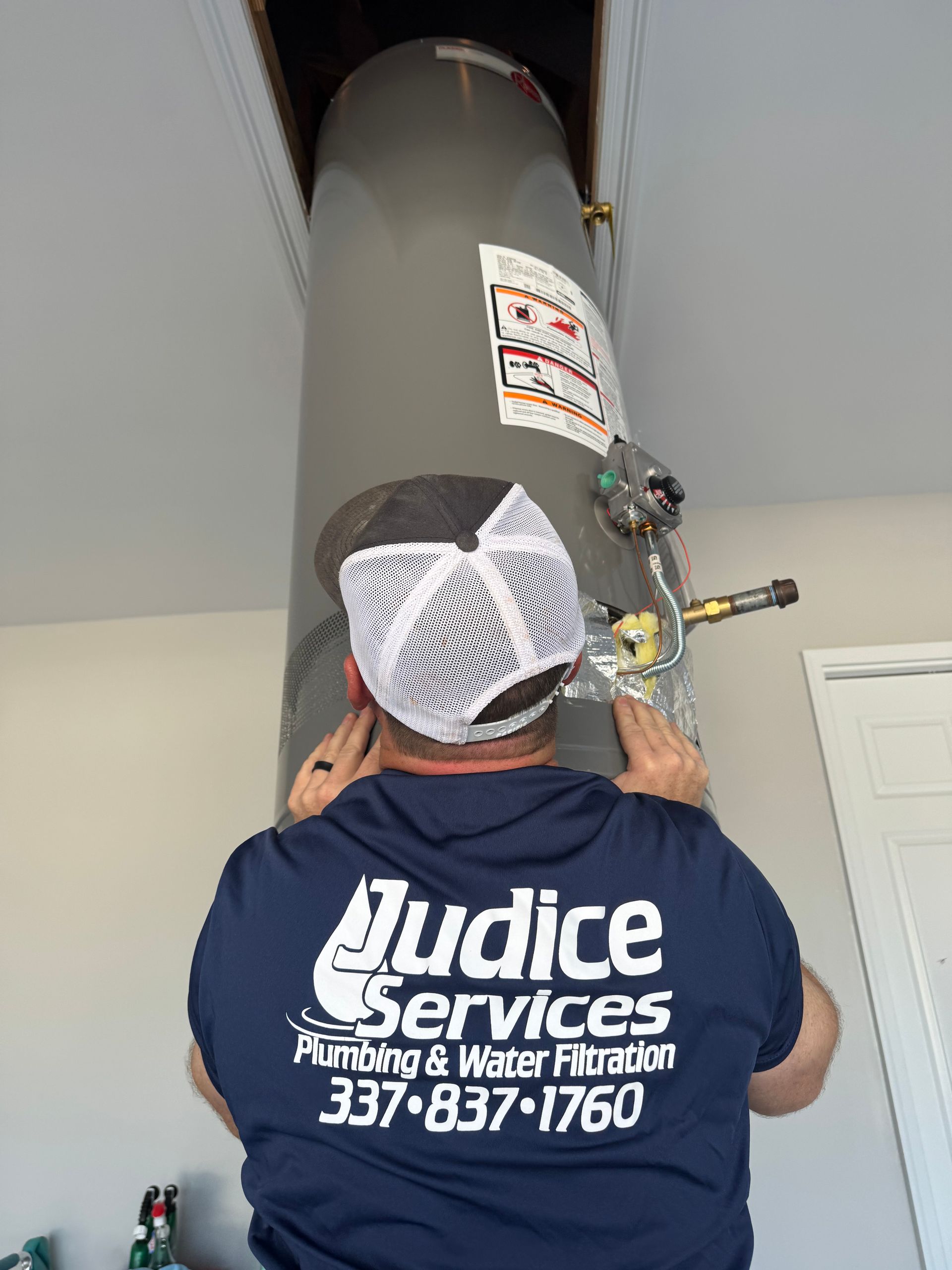 Plumber in blue shirt, installing a water heater in an attic.