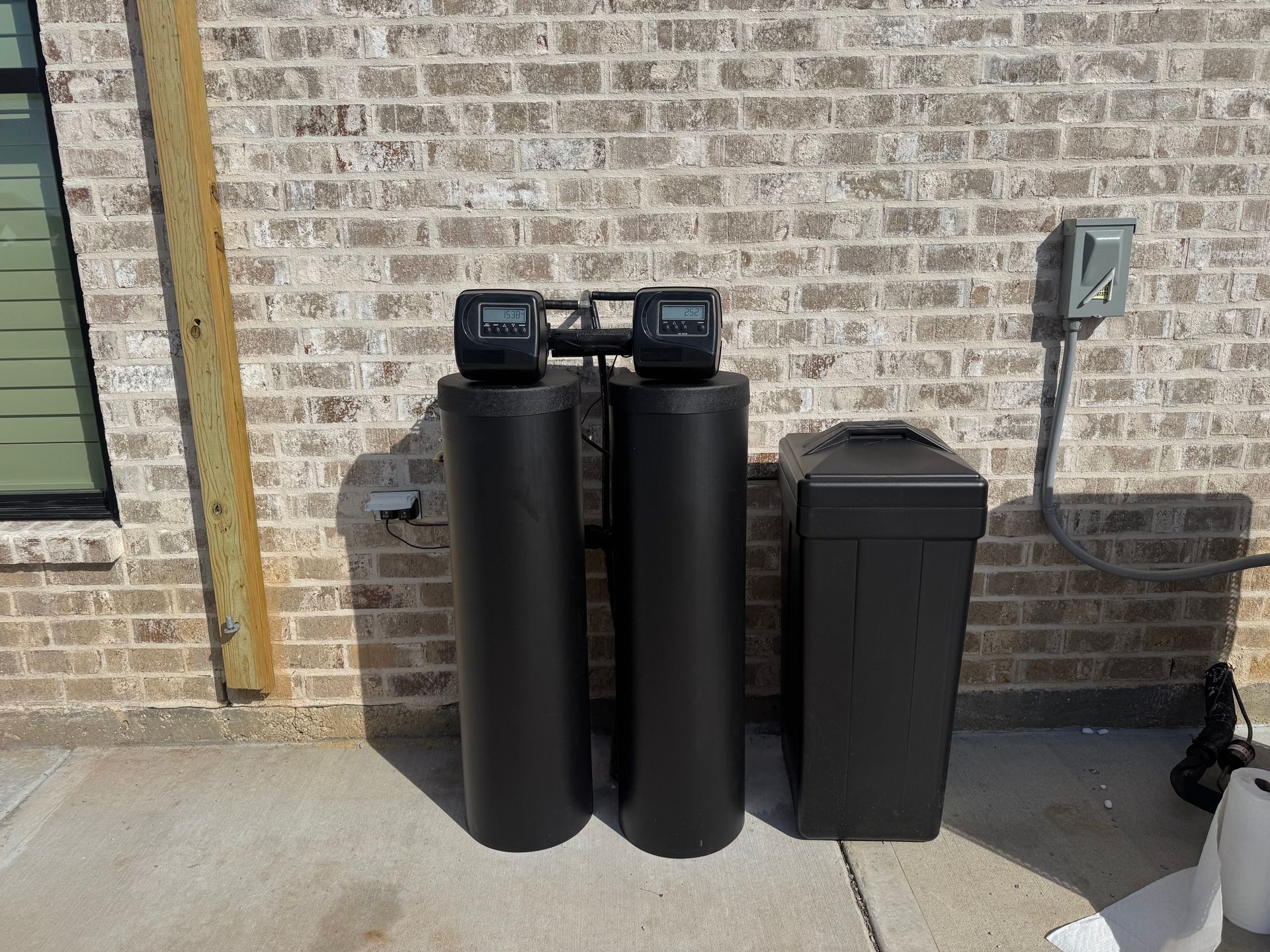 Four beige water filtration tanks with black control panels, connected to green pipes.