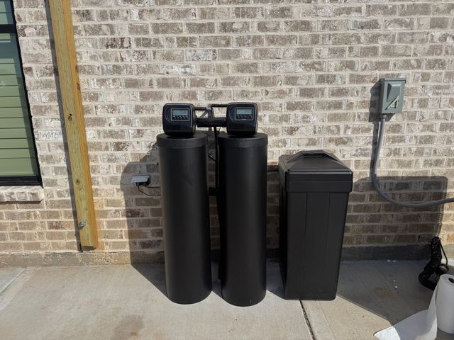 Water filtration system with four cylindrical tanks, blue pipes, and a large blue water tank in the background.