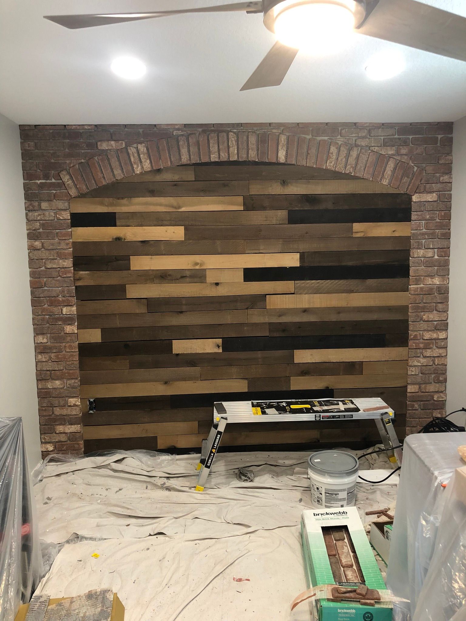A rustic brick archway frame surrounds a wall featuring horizontal, reclaimed wood planks of varying brown tones.