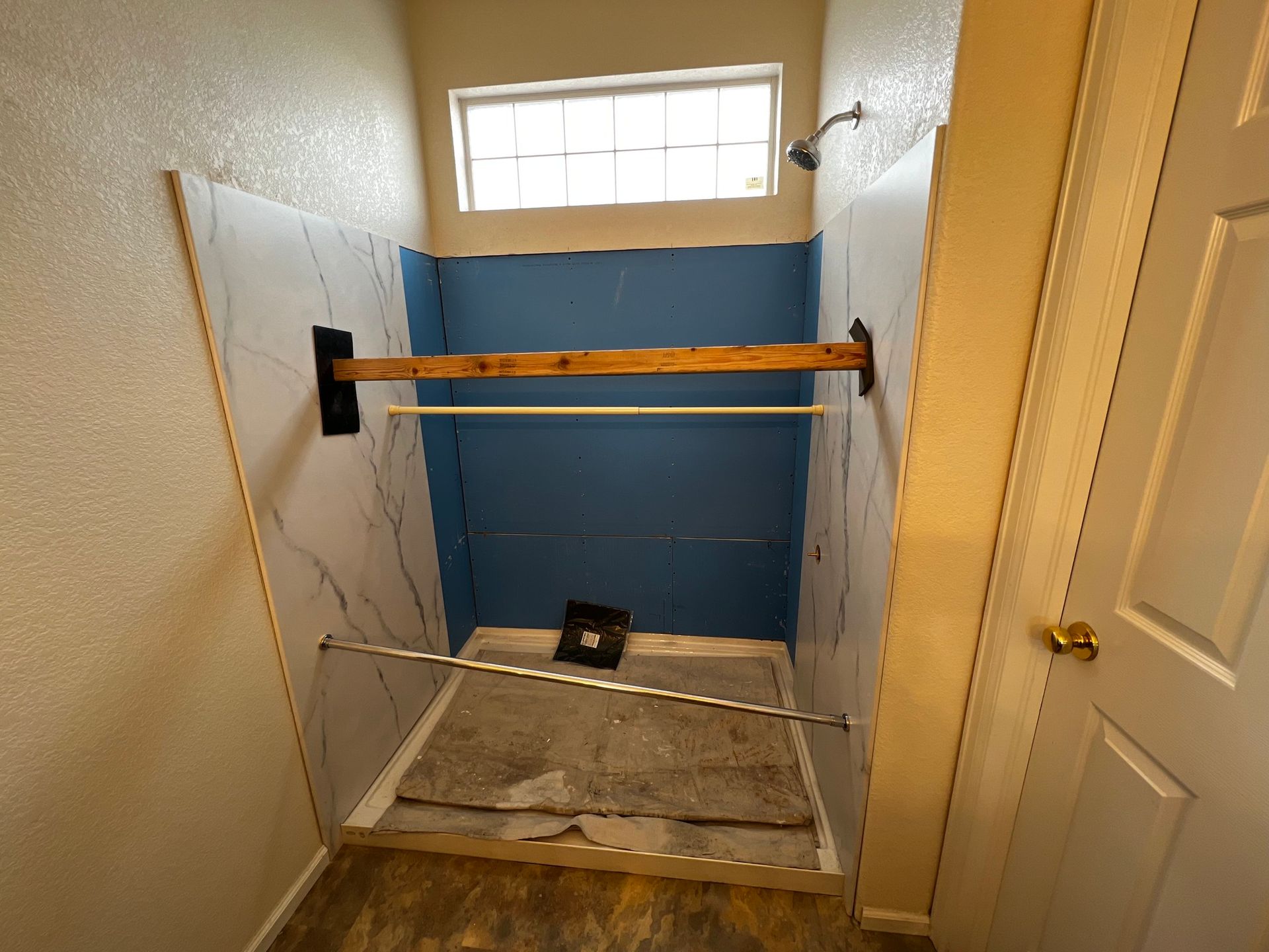 A shower stall undergoing renovation with marble-patterned wall panels installed over blue waterproof backer board.