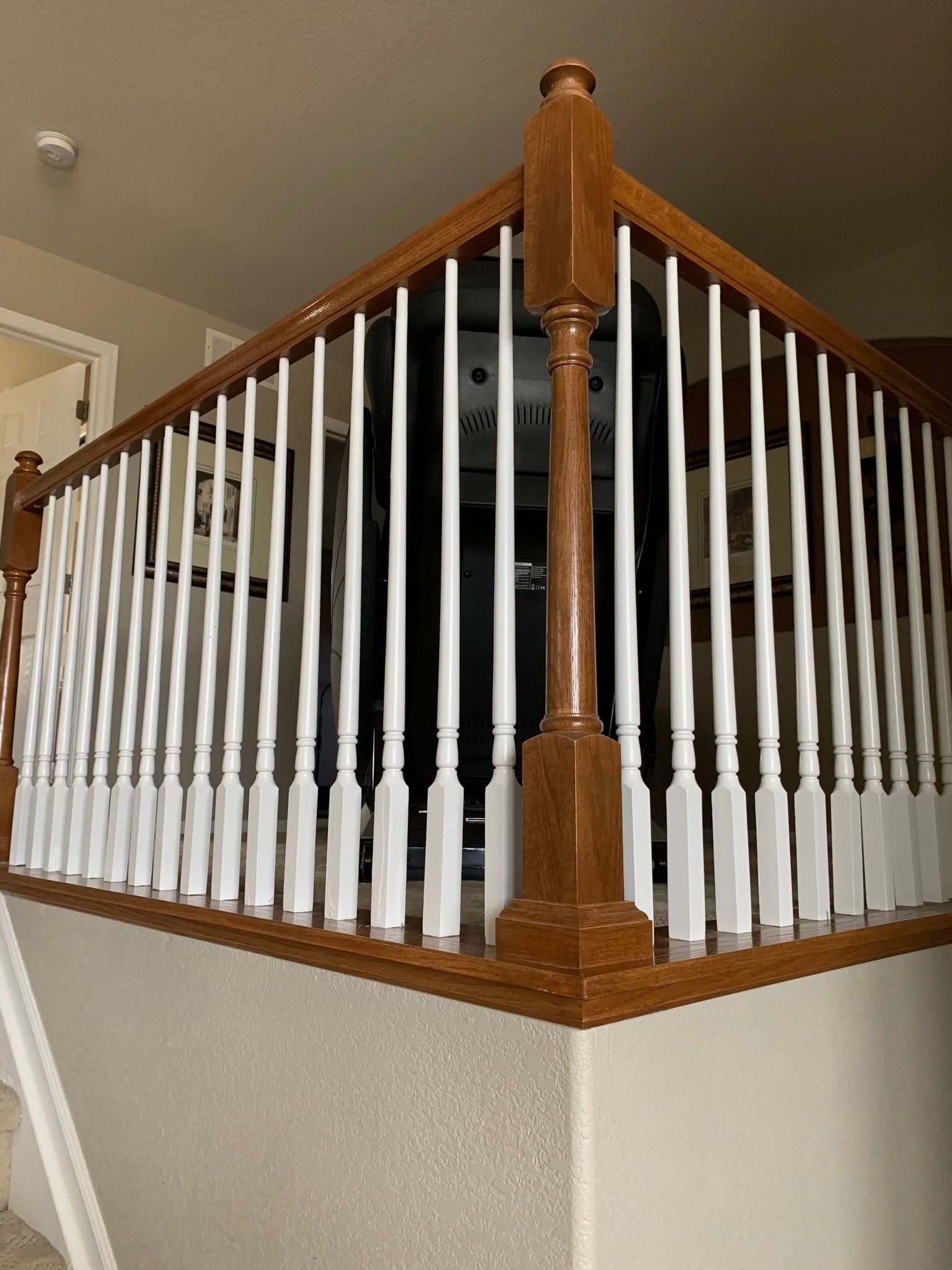 A wooden staircase railing with white vertical balusters on a landing corner inside a house.