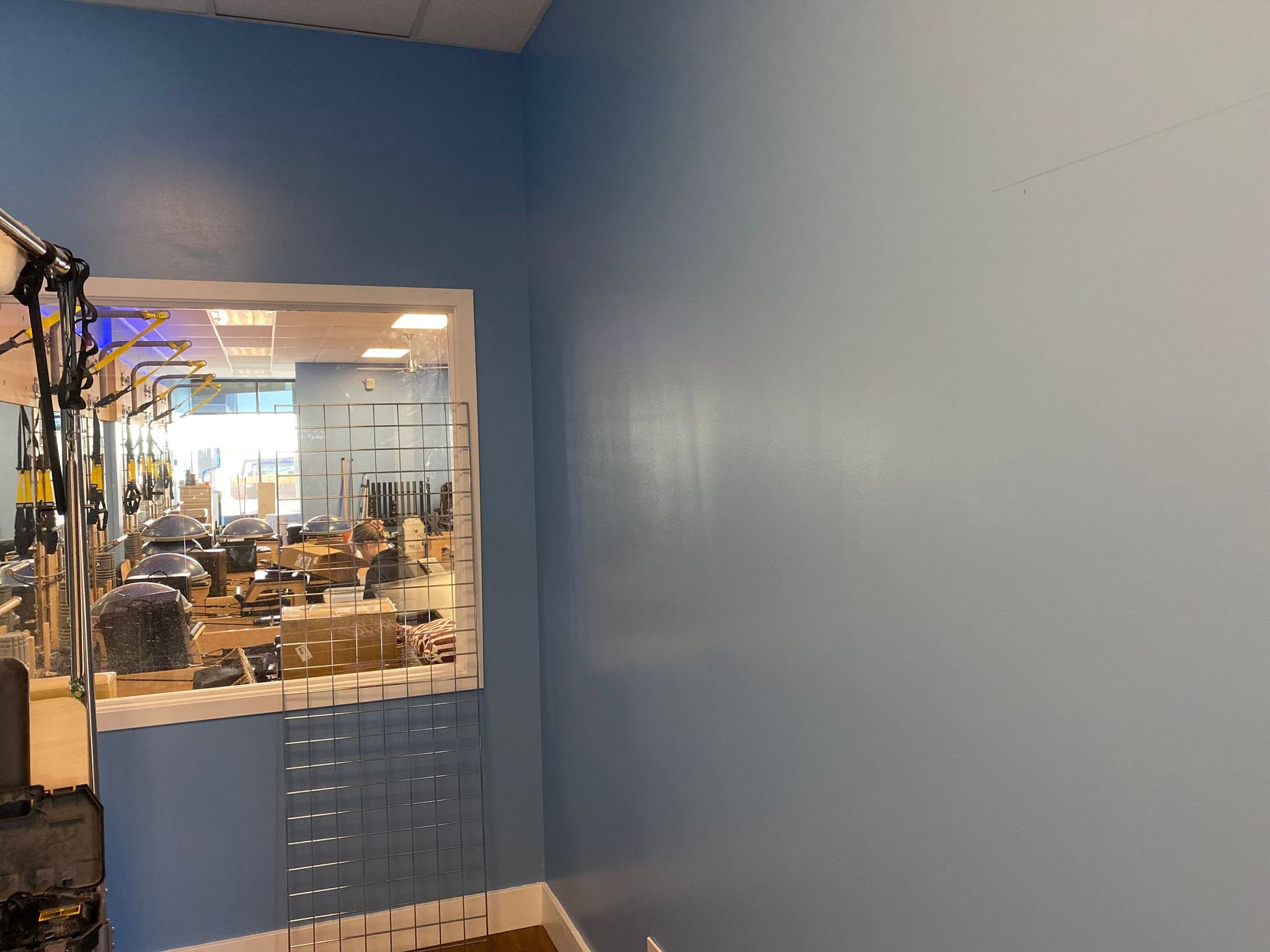 A blue-walled room with a window looking into a hair salon featuring styling chairs and equipment.