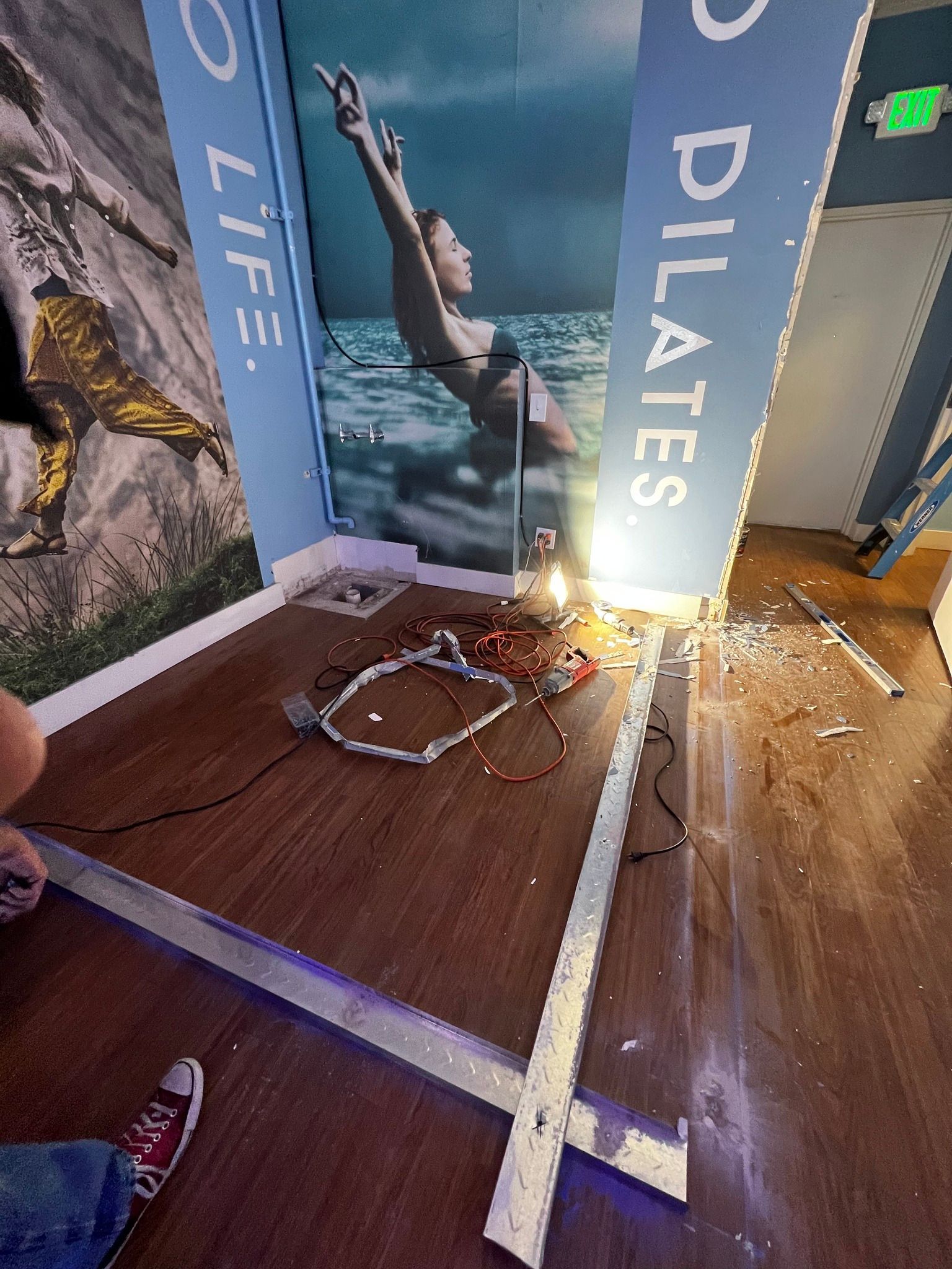 Damaged Pilates studio wall panels and debris on the floor, with sunlight streaming in.