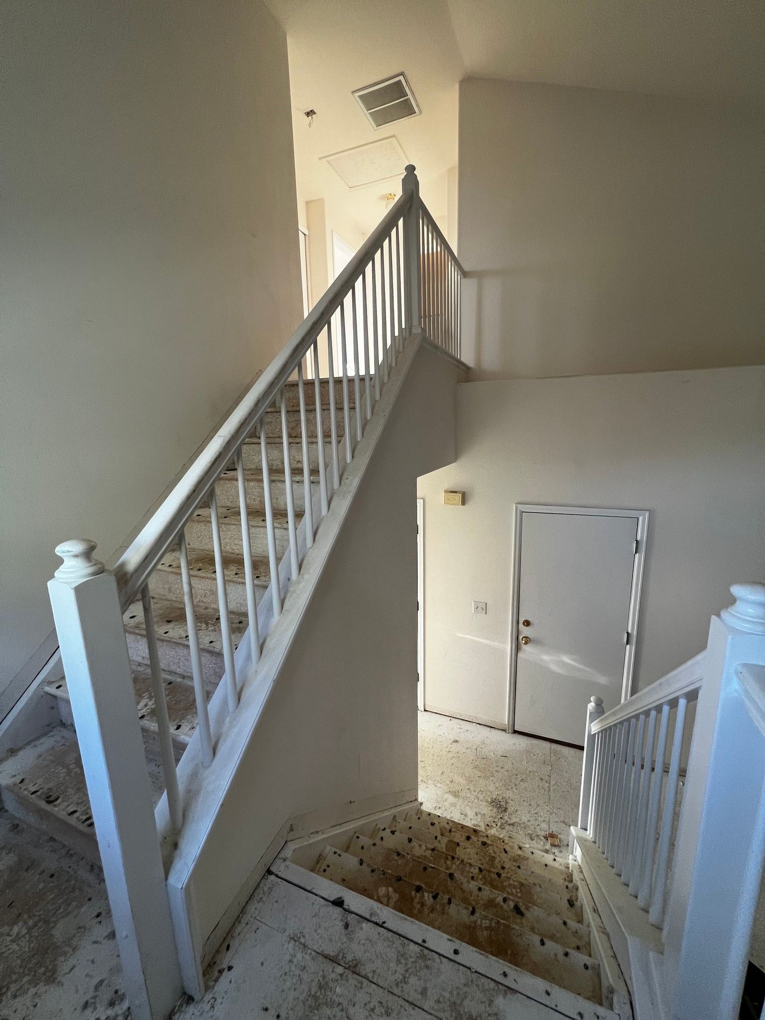 A white staircase with a wooden railing leading upward in a bright, modern interior hallway with a door below.