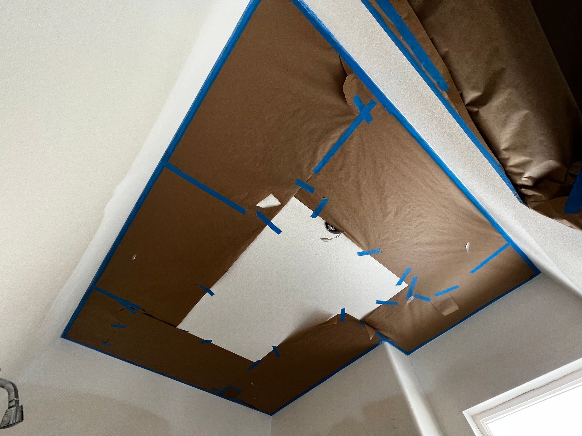 Brown paper masking covering a ceiling area, with blue painter's tape outlining the section being prepared for painting.