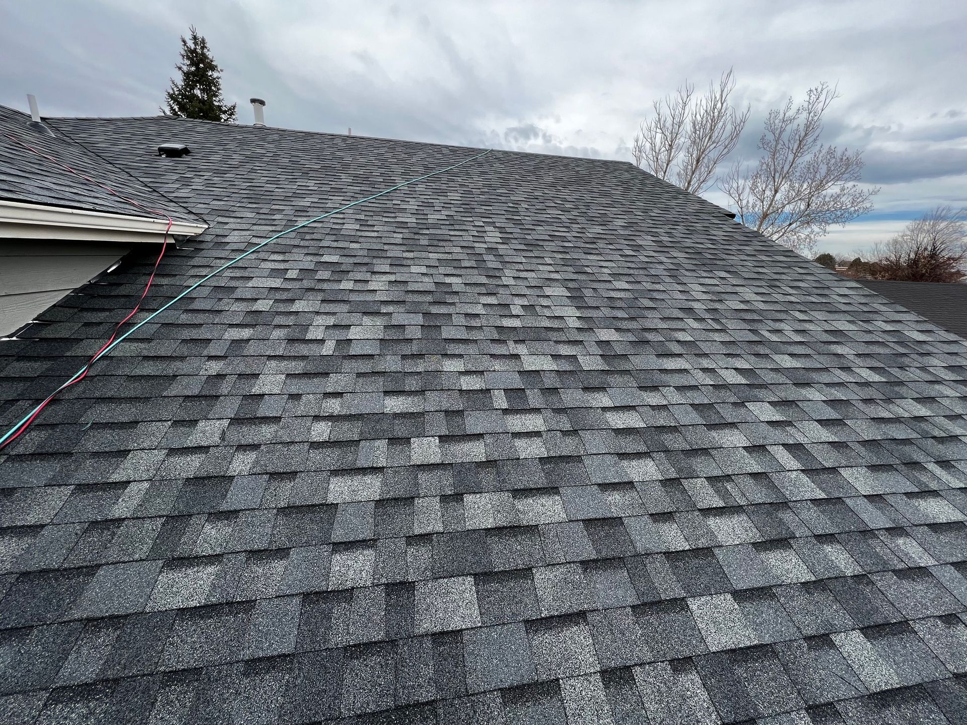 A high-angle view of a grey architectural asphalt shingle roof under a cloudy sky.