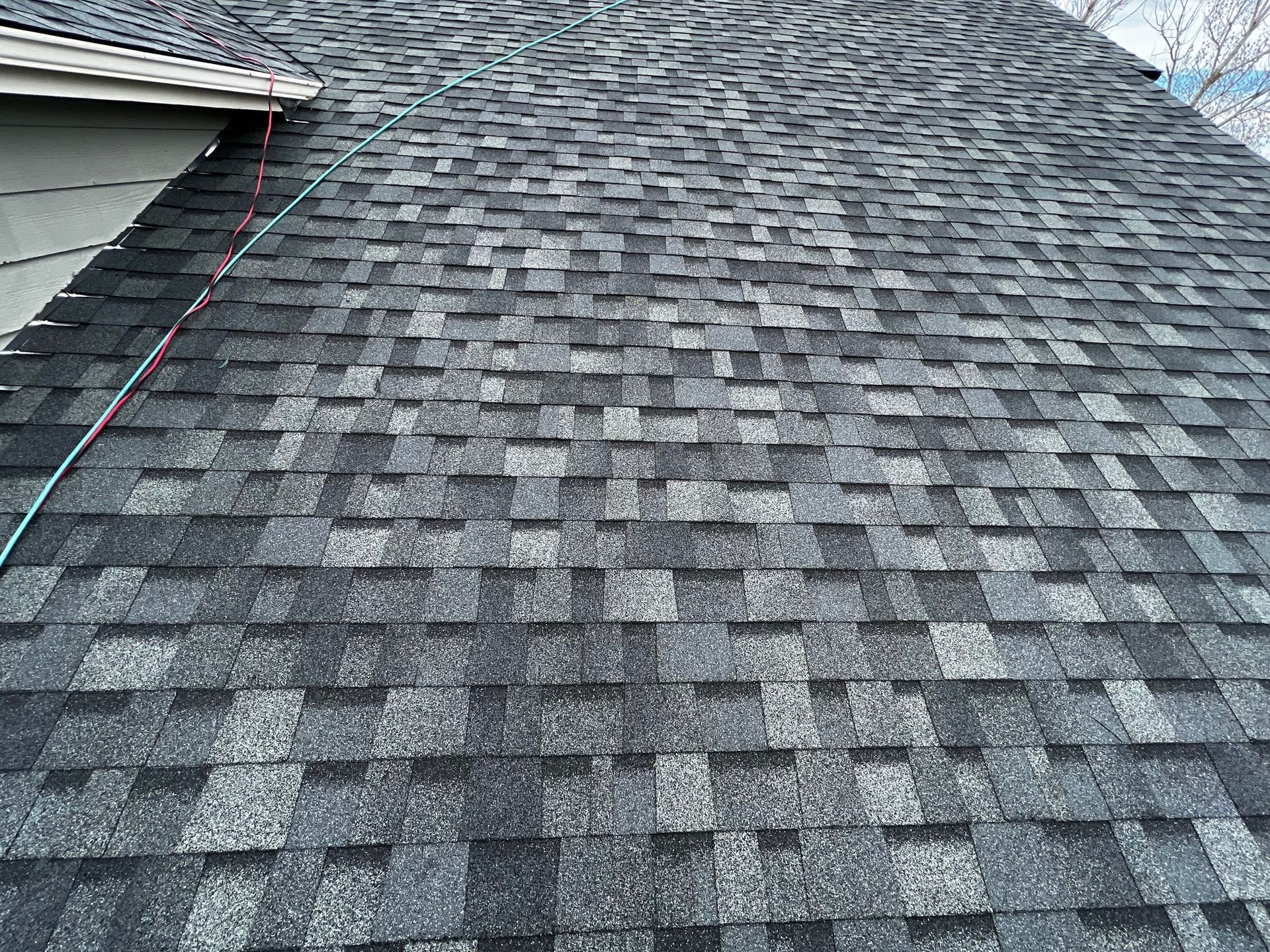 A high-angle view of a grey and black asphalt shingle roof showing the pattern and texture of the material.