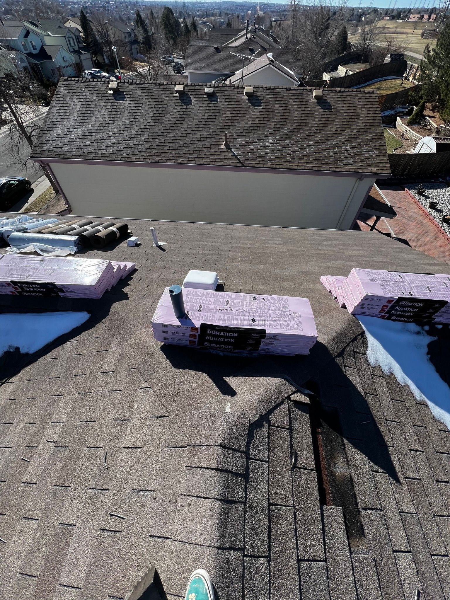 Snow-covered rooftop with several small ventilation units and a residential neighborhood in the distance