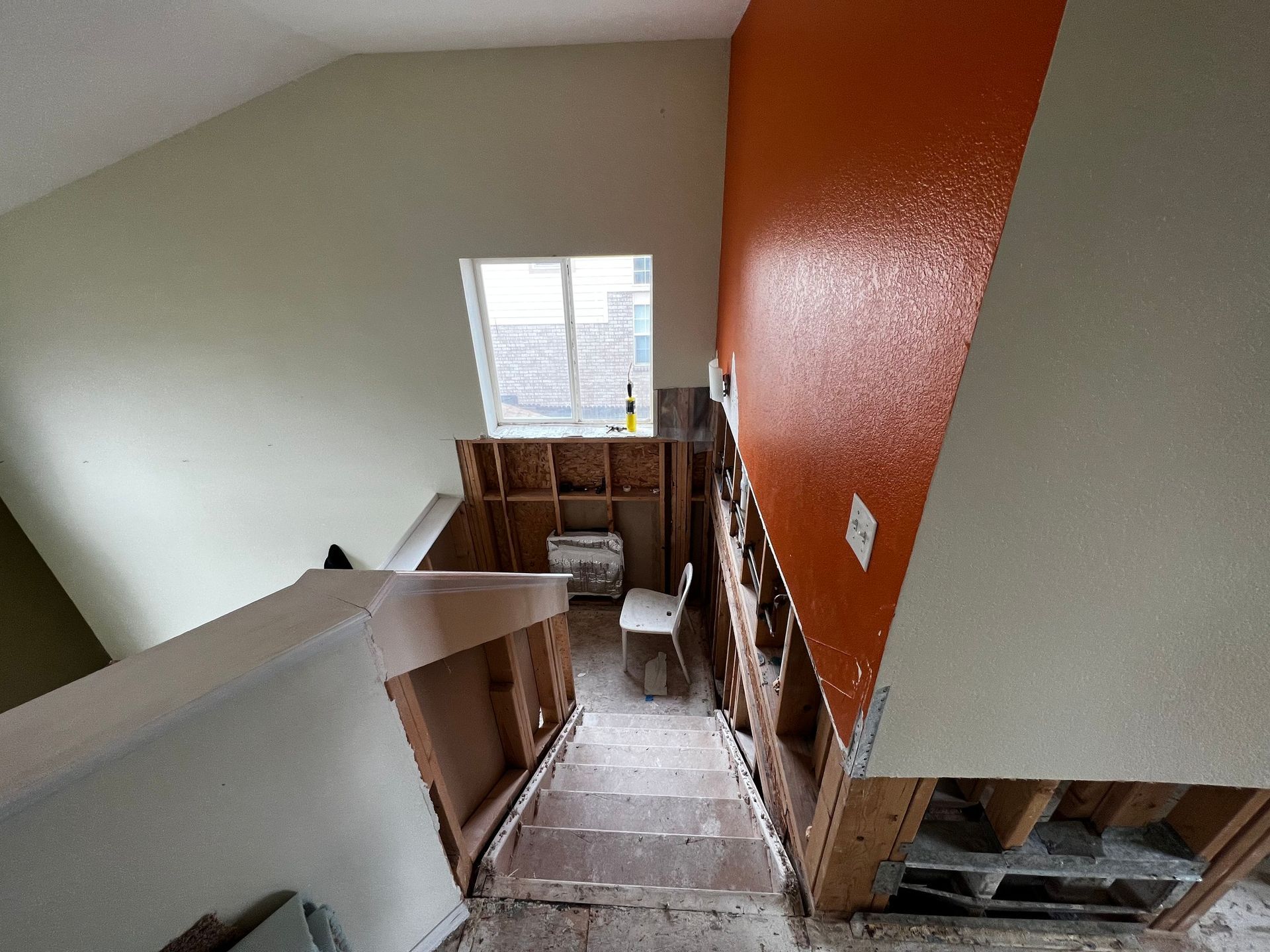 Staircase under renovation, showing exposed wooden studs, missing railings, and a window at the bottom of the landing.