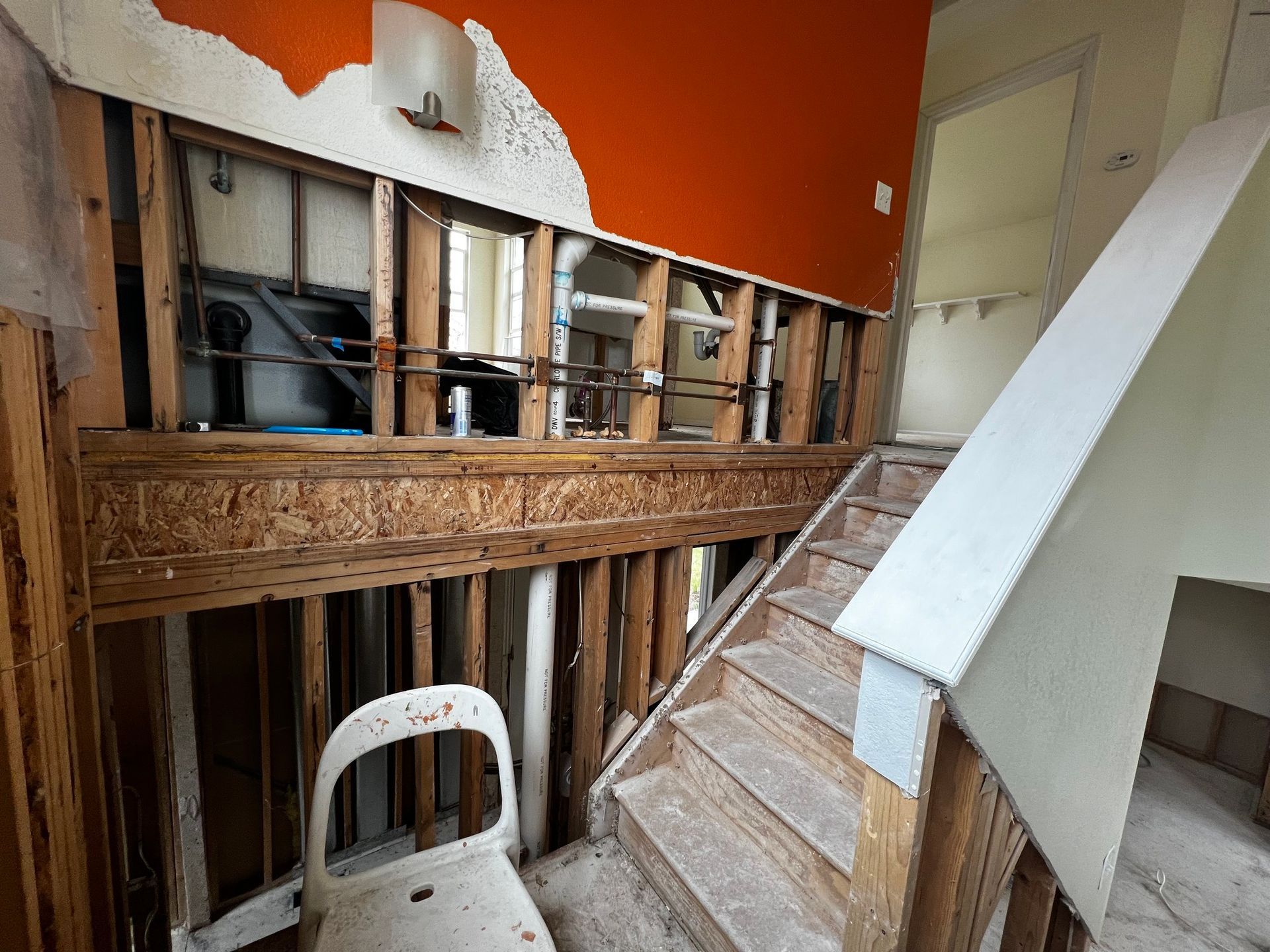 Construction site with an open wall revealing wooden studs and pipes next to a staircase.