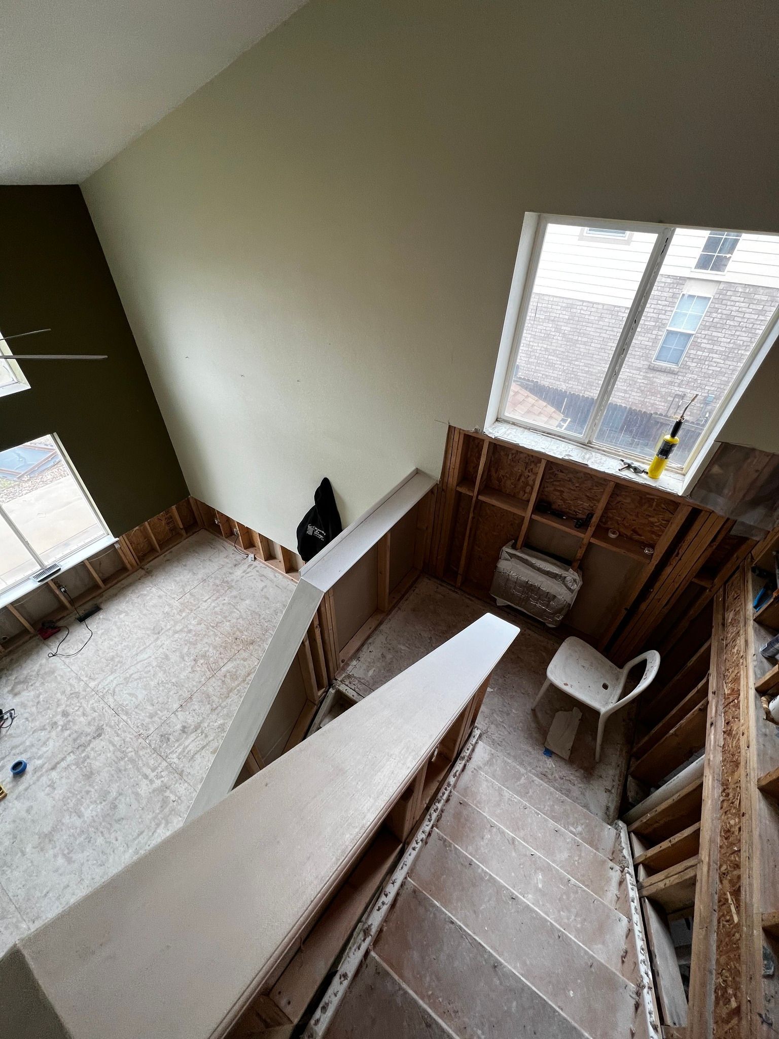 A high-angle view of a room under construction with exposed wooden wall studs, plywood flooring, and a window.
