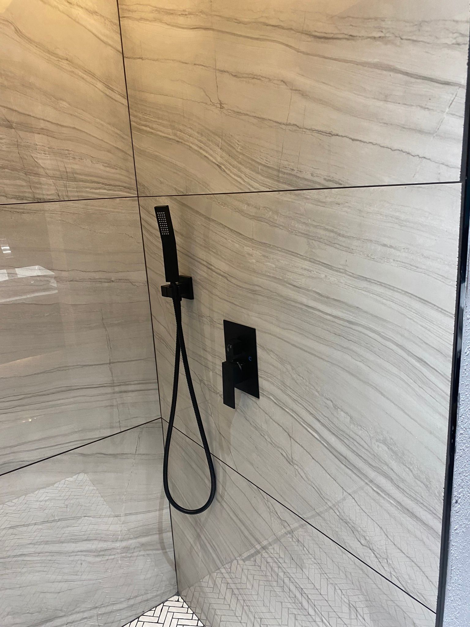 A modern shower features light grey, horizontally-veined tile walls, black plumbing fixtures, and a black handheld shower.