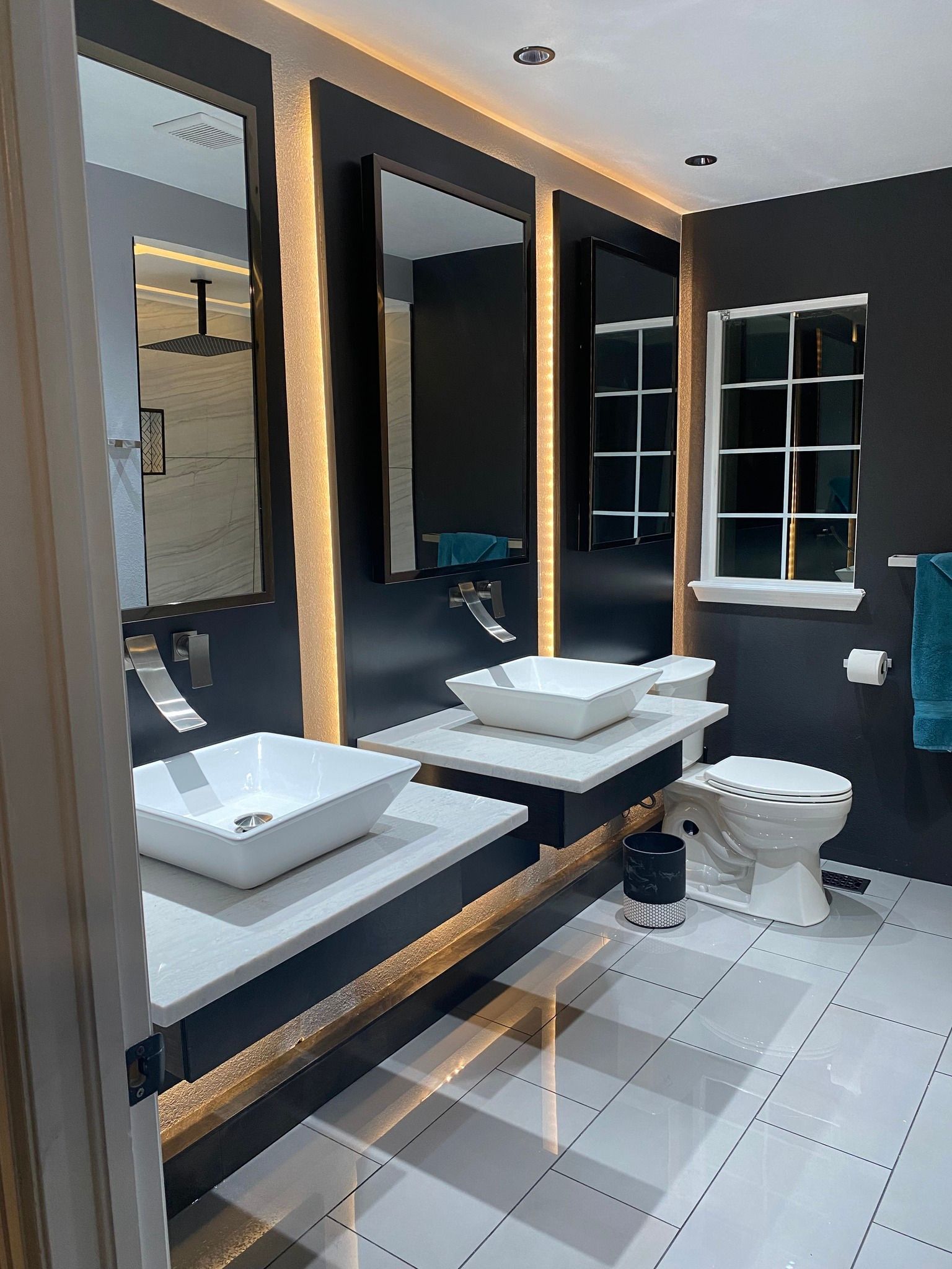 Modern bathroom with two white vessel sinks on gray floating vanities, backlit mirrors, and a white toilet.