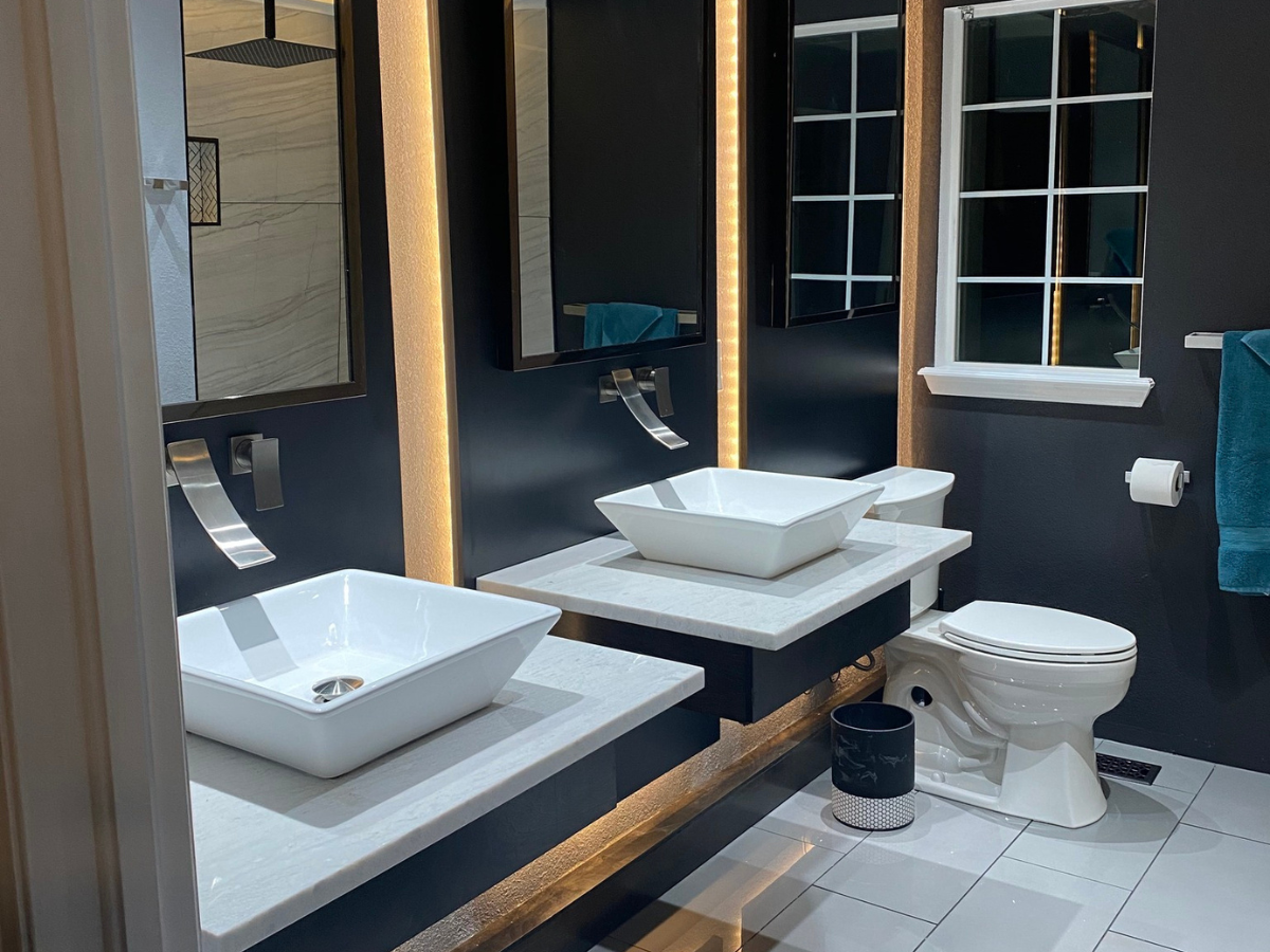 A modern bathroom vanity with dual vessel sinks, floating white countertops, dark cabinetry, and a white toilet.