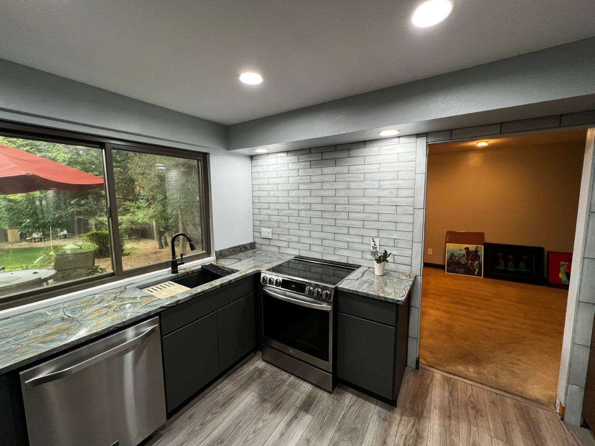 Modern kitchen with dark cabinetry, granite countertops, stainless steel appliances, and a gray brick backsplash.