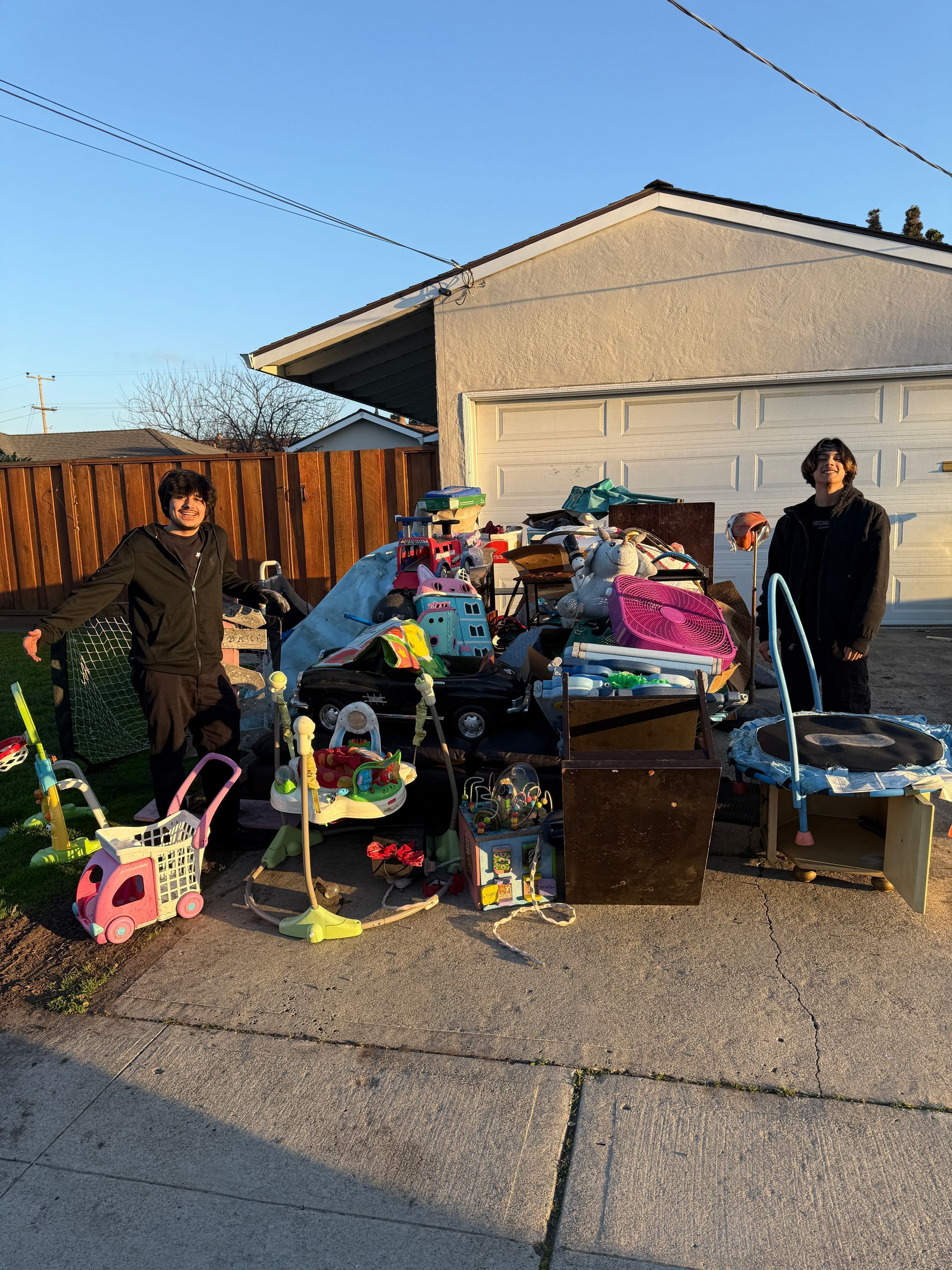Two people are standing in front of a pile of junk in front of a house.