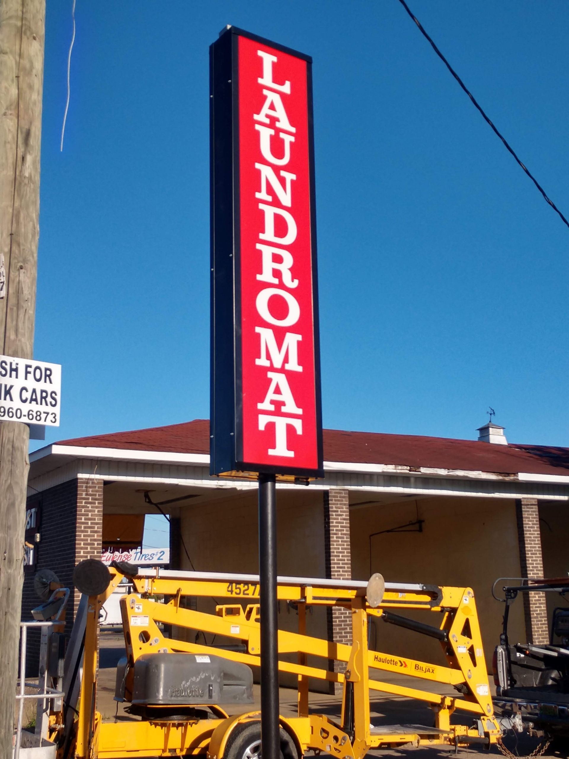 A laundromat sign with a yellow lift in front of it